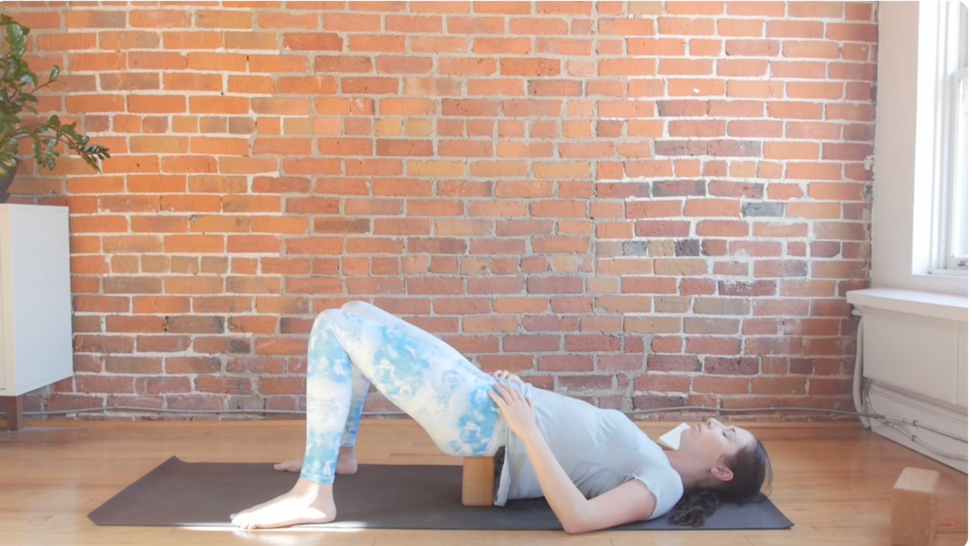 Woman lying on a yoga mat with a block beneath the sacrum