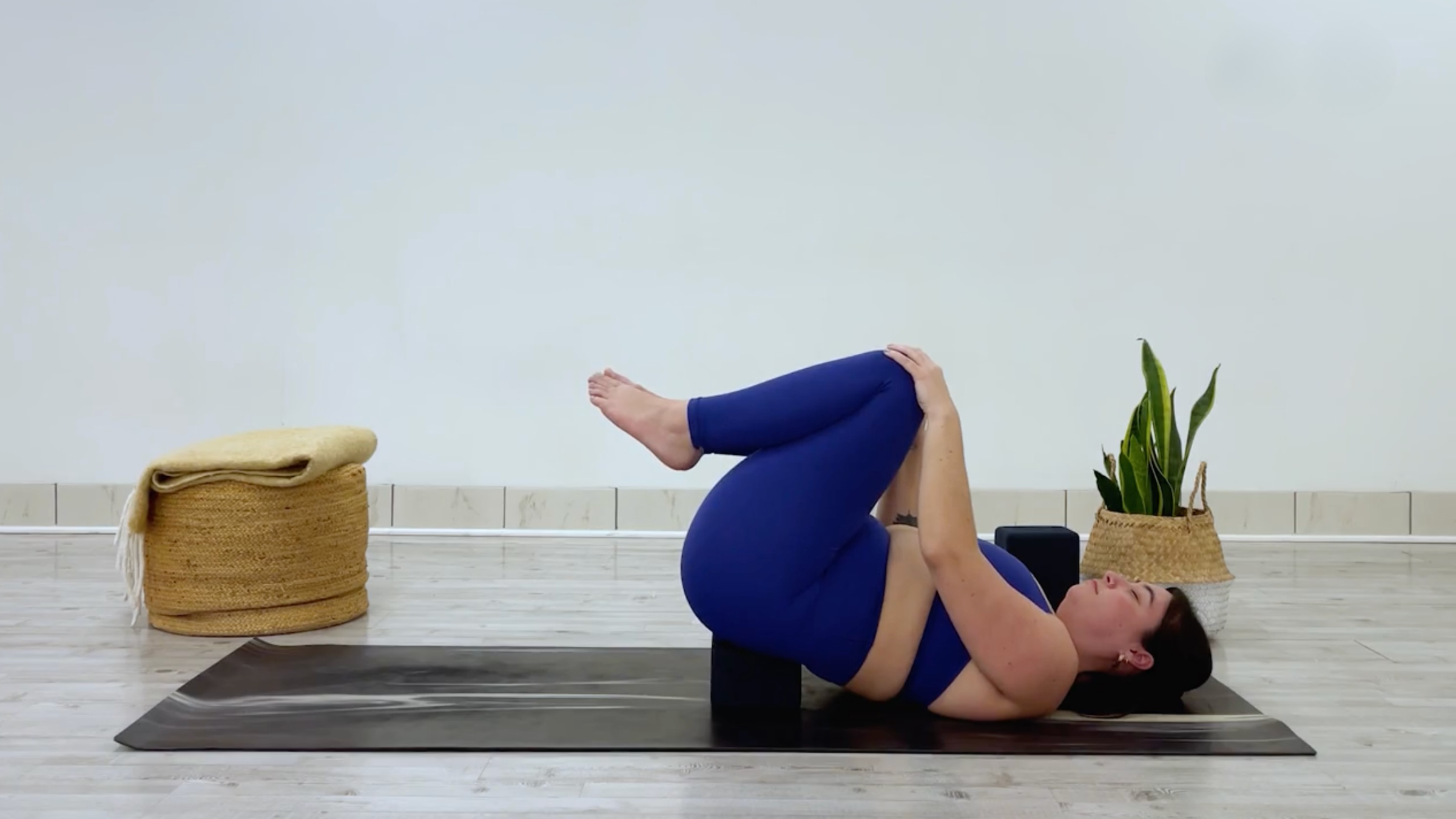 Yoga teacher Taylor Lorenz is in a knees-to-chest position, doing a yin yoga pose to stretch her inner thighs.