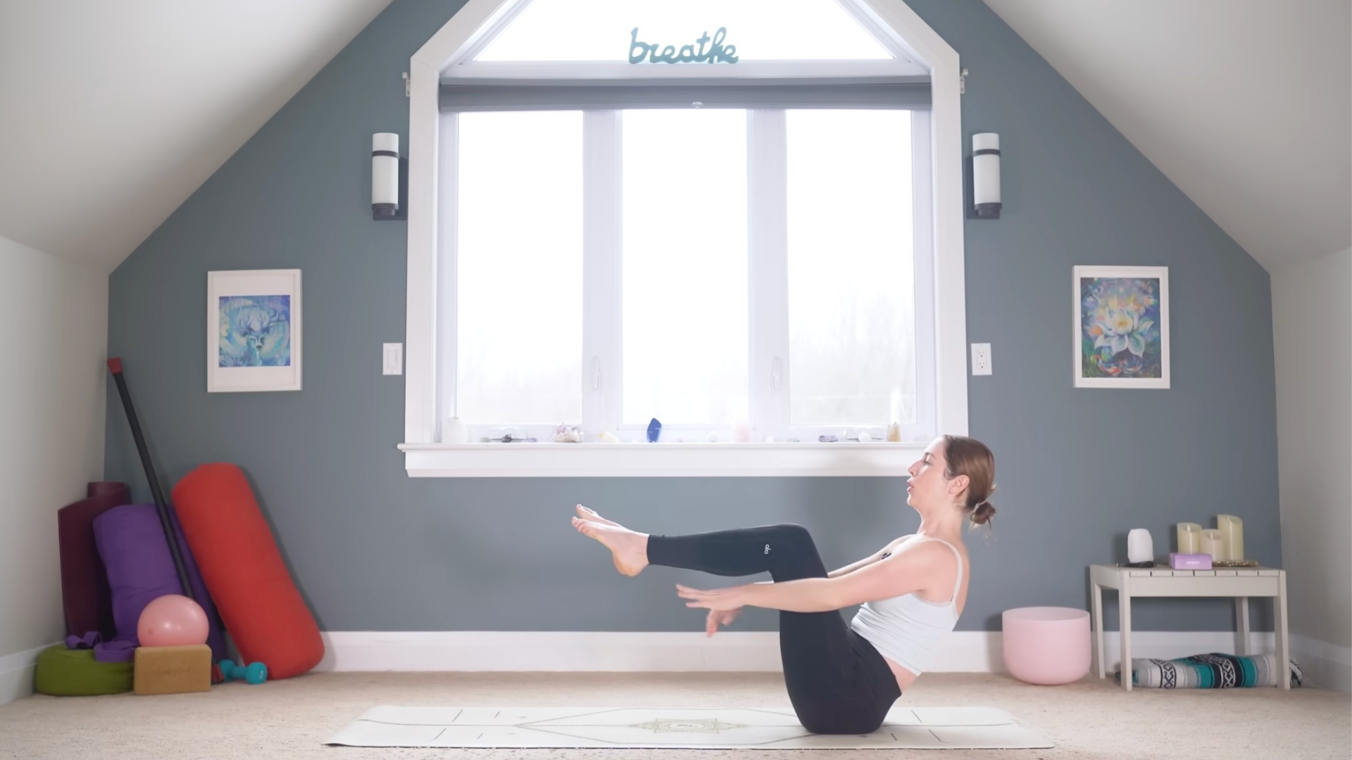 Woman sitting on a yoga mat with her legs lifted and her arms reaching forward in Boat Pose