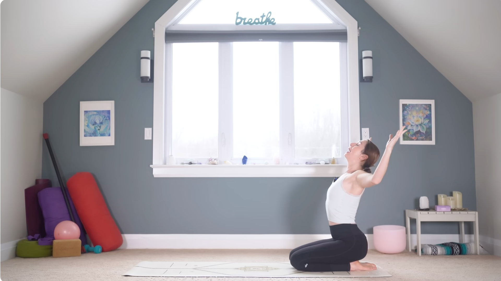 A woman kneels on a yoga mat while sitting on her heels and doing a slight backbend