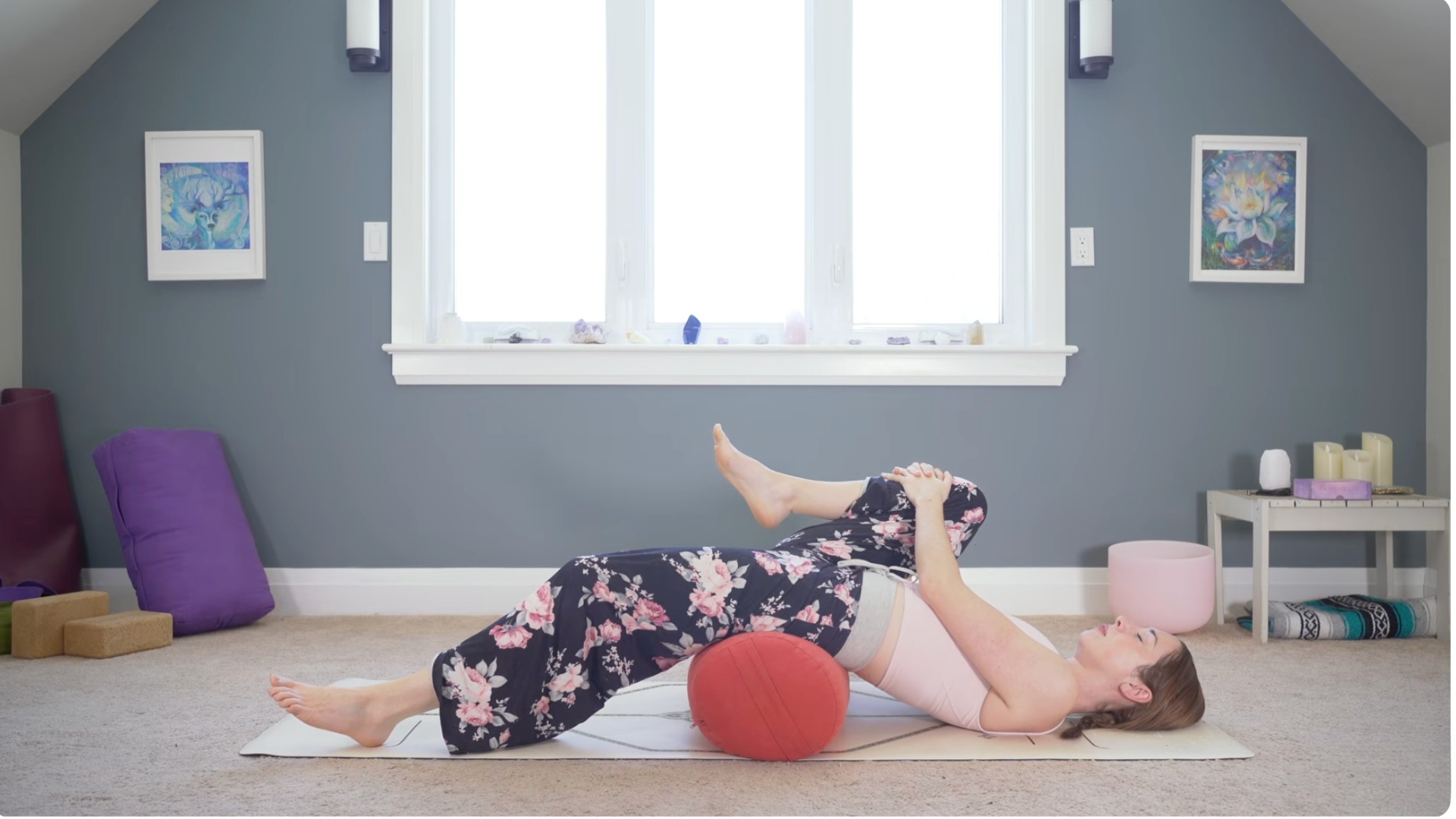 Woman lying on her back drawing her right knee toward her chest in a hip flexor stretch during yin yoga