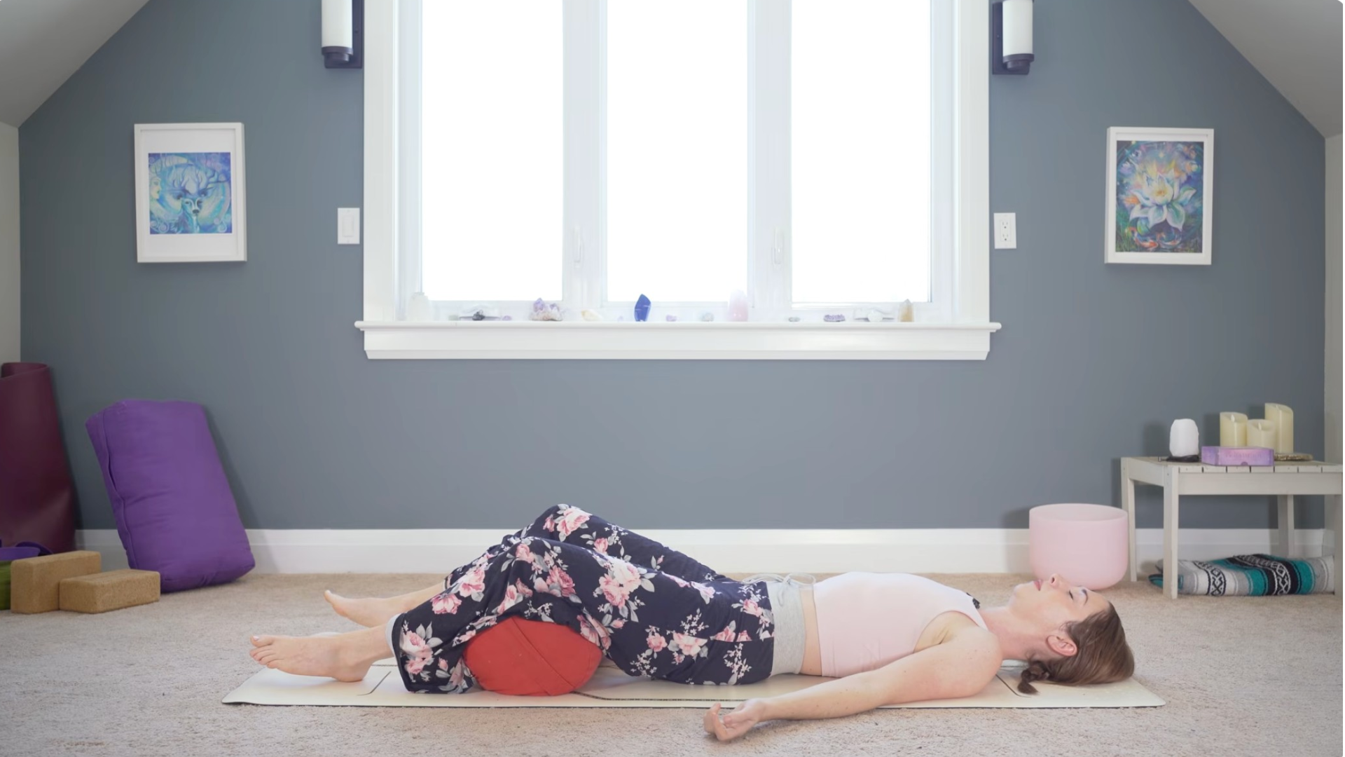 Woman lying on a yoga mat in Savasana with a bolster beneath her knees