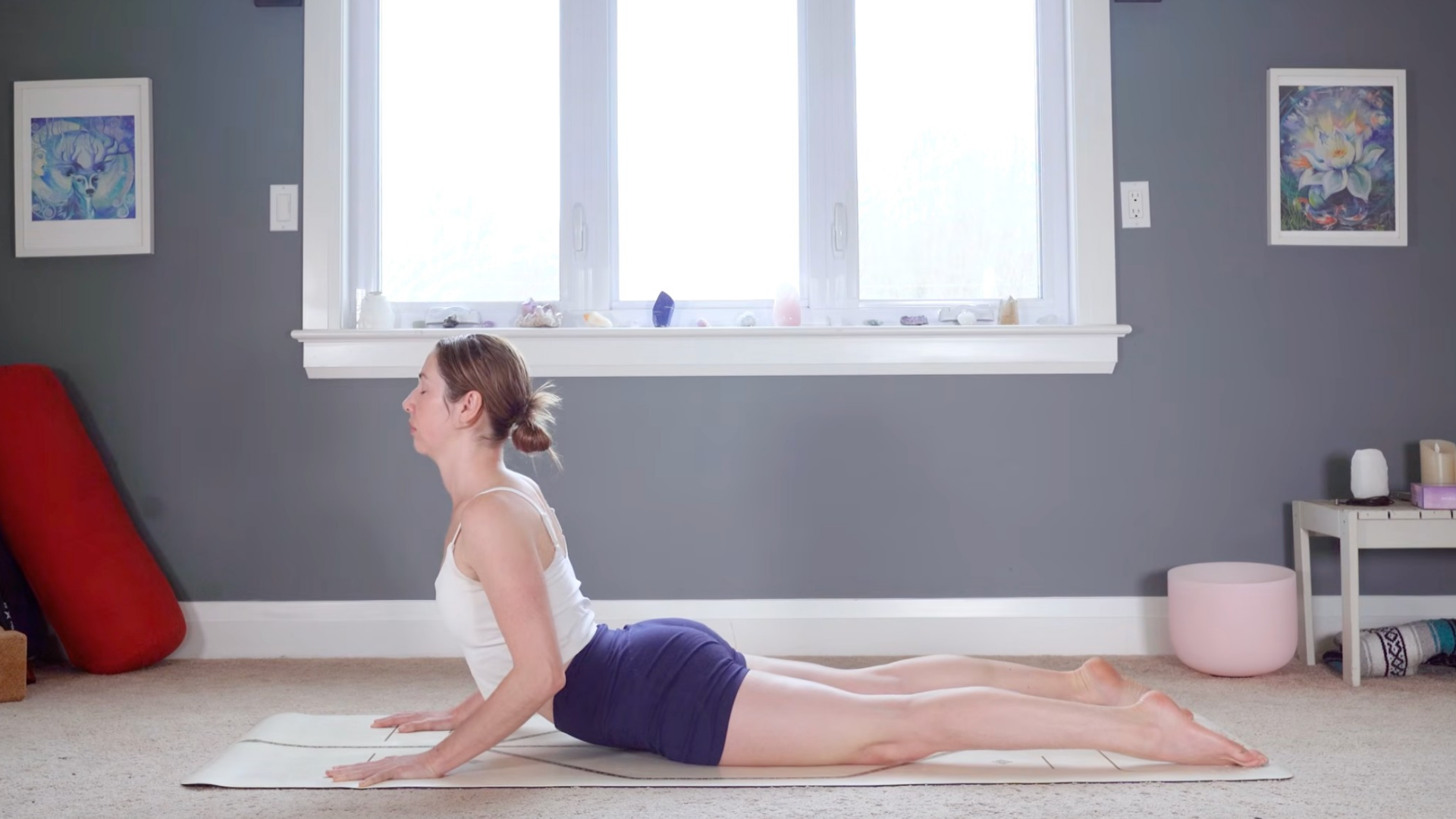 Woman lying on her belly on a yoga mat and lifting her chest in Cobra Pose