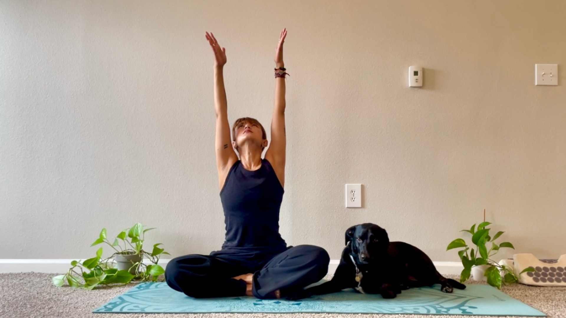 Woman sitting cross-legged on a mat practicing an accessible seated version of Upward Salute or Urdhva Hastasana
