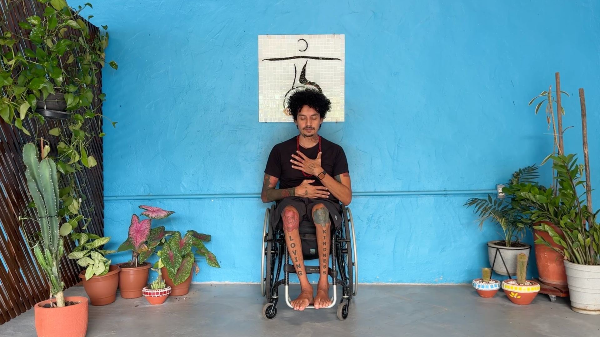 Yoga teacher seated in a wheelchair with one hand on his heart and the other on his belly as he meditates