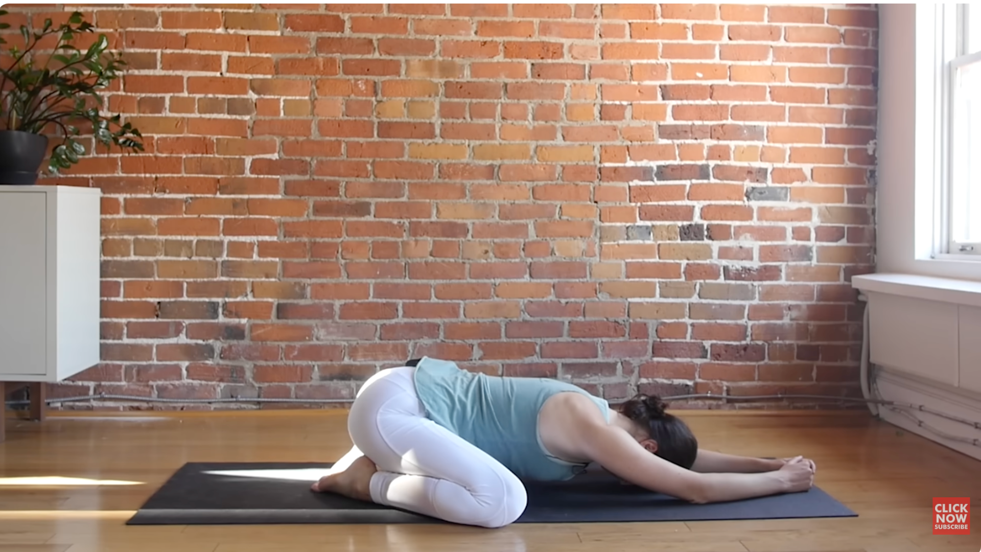 A woman kneels on a yoga mat in the passive forward bend known as child's pose (balasana).