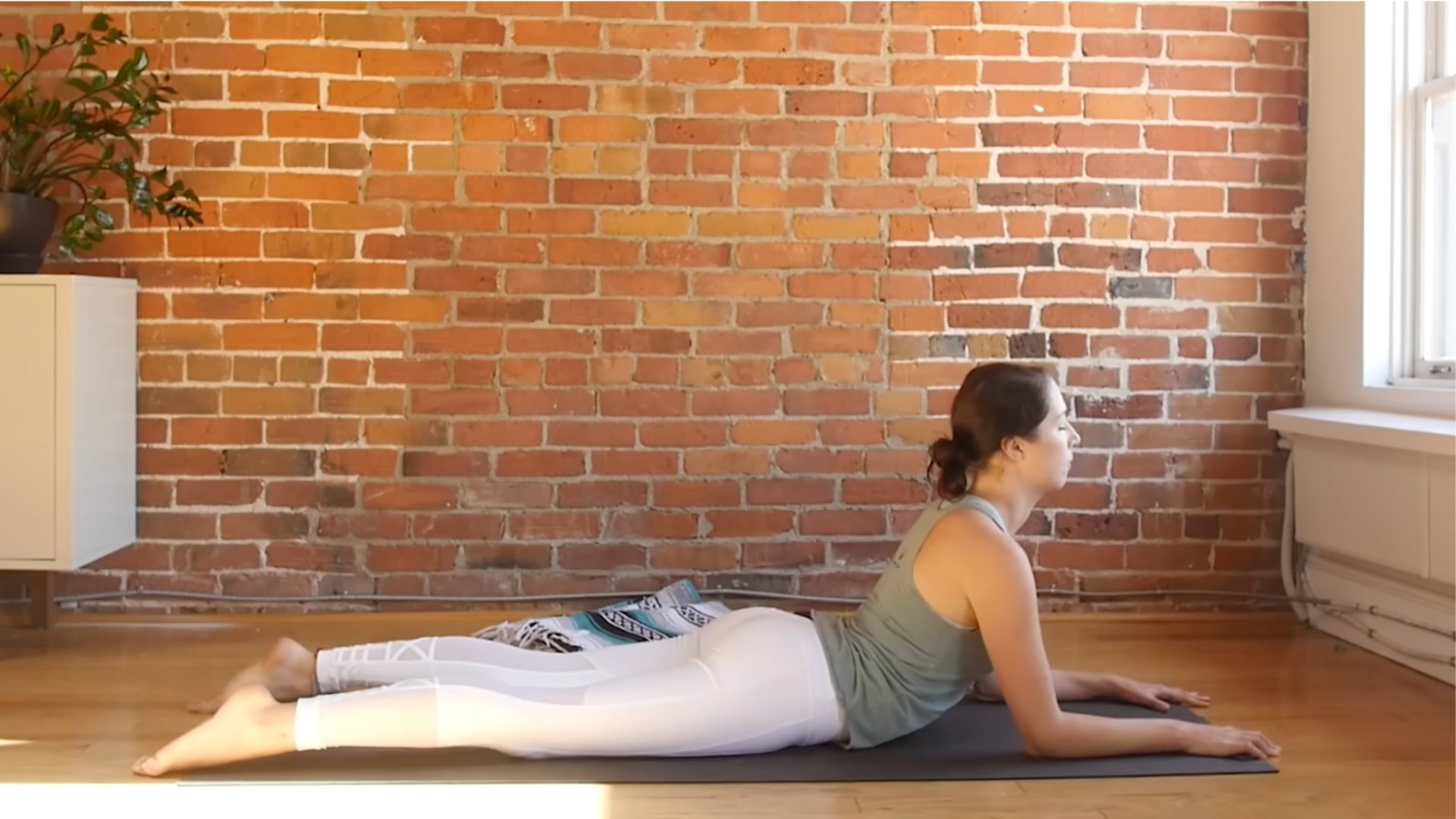 Woman lying on the belly on a yoga mat with her forearms on the mat propping up her chest in the passive backbend known as Sphinx