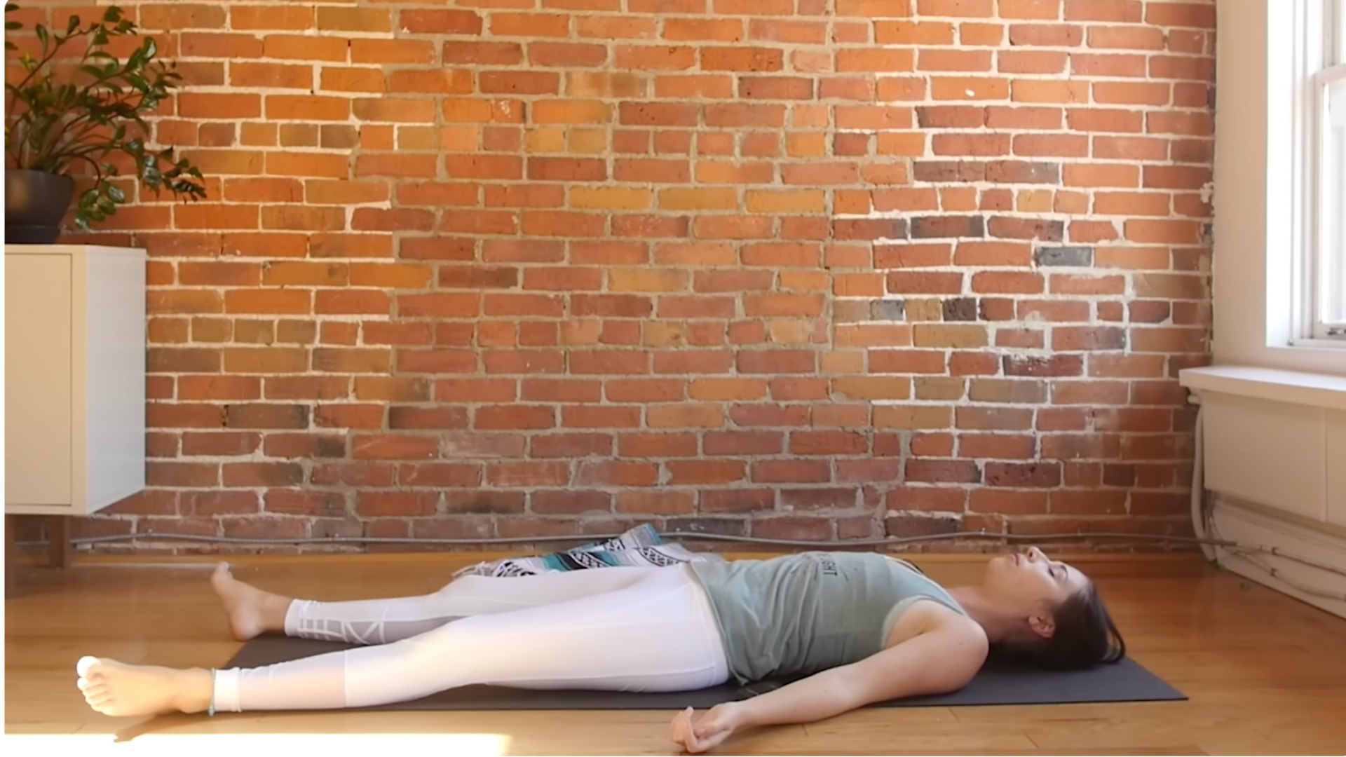 Woman lying on her back in Savasana or Corpse Pose, the final resting pose after a yoga practice