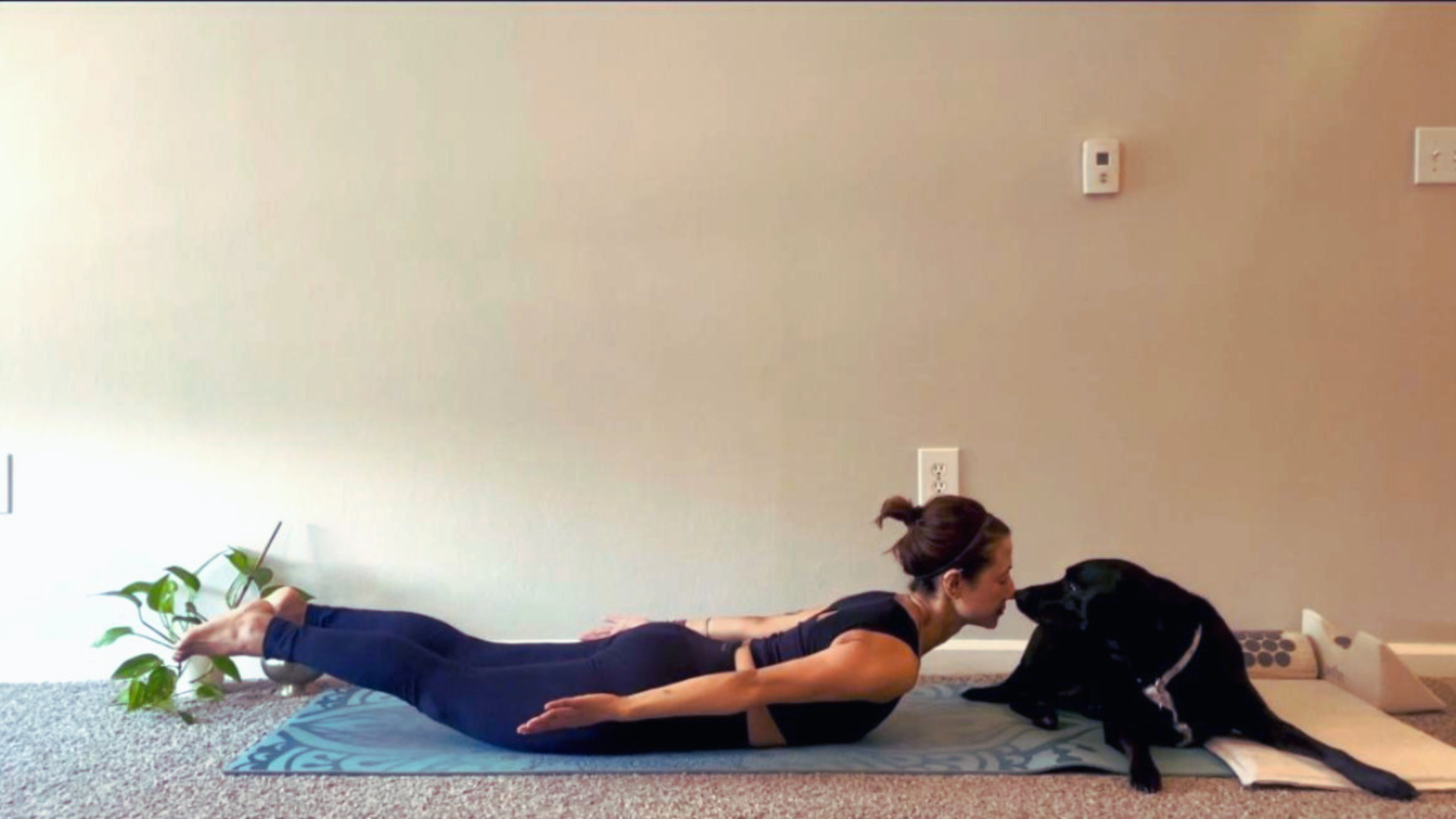 Woman lying on her belly on a yoga mat while lifting her legs and chest in Locust Pose