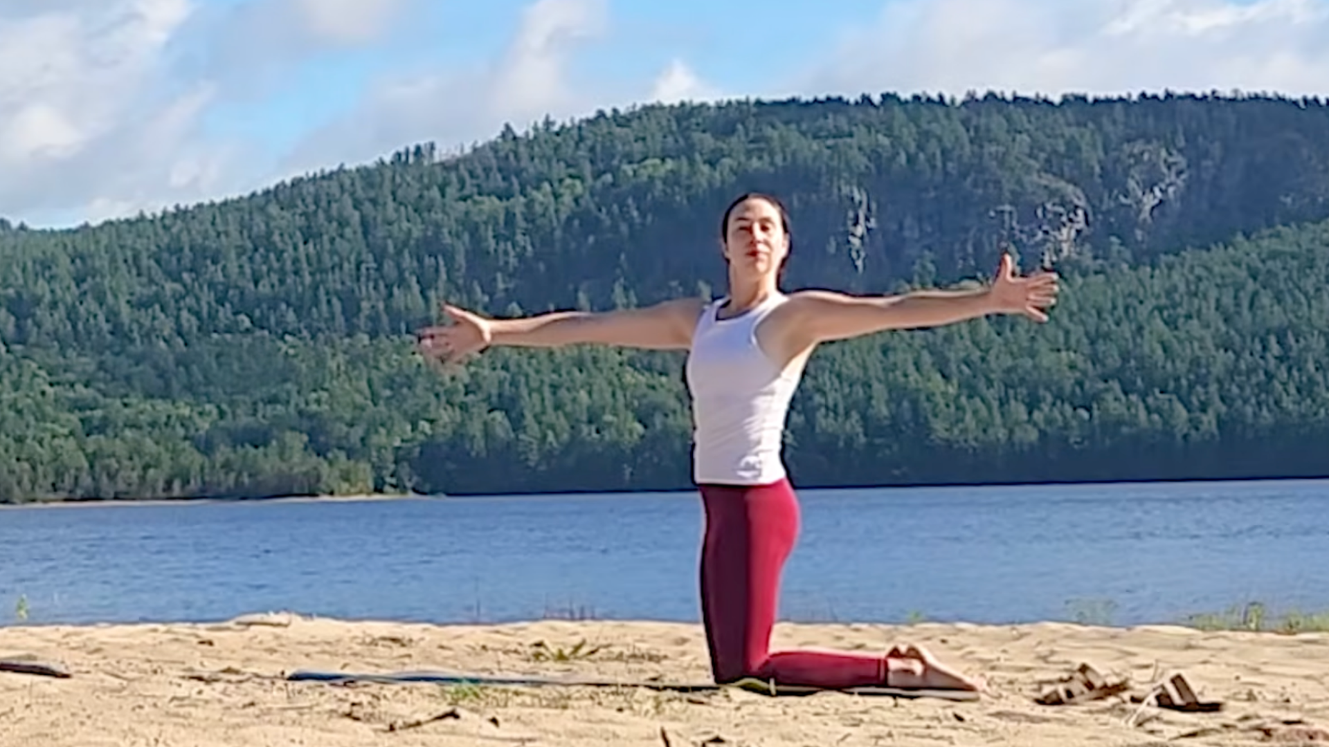 Teacher kneeling on a mat during a 15-minute yoga for your back routine with her arms outspread