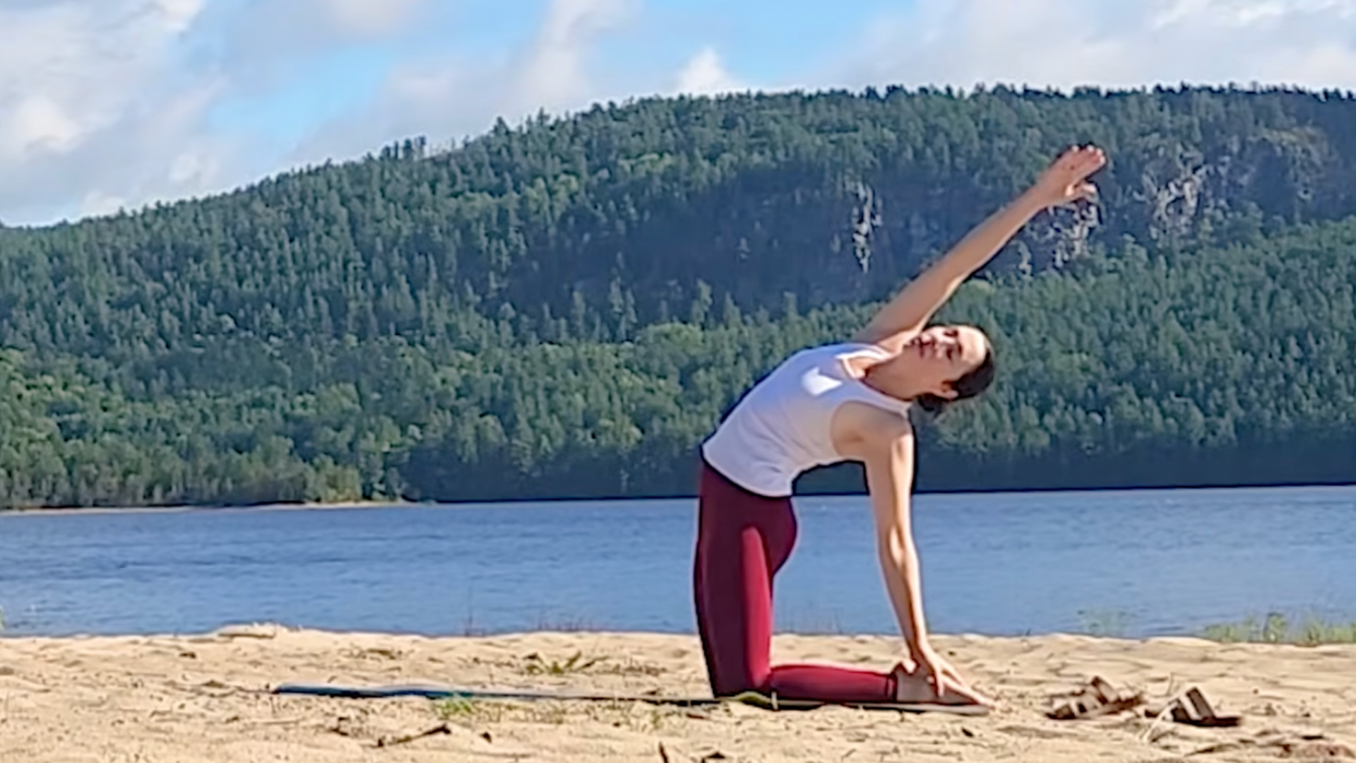 Woman kneeling in Half Camel Pose by sweeping one arm behind her and the other arm overhead