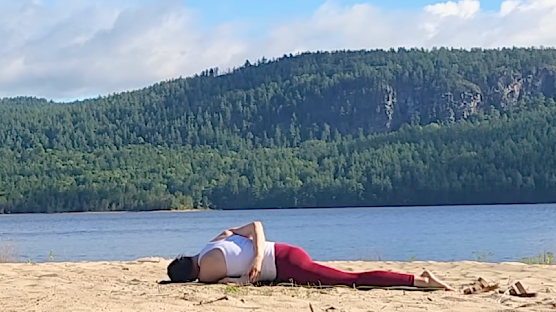 Woman lying on her belly in Pigeon Pose (Eka Pada Rajakapotasana) with her arm wrapped behind her back in a Half Bind