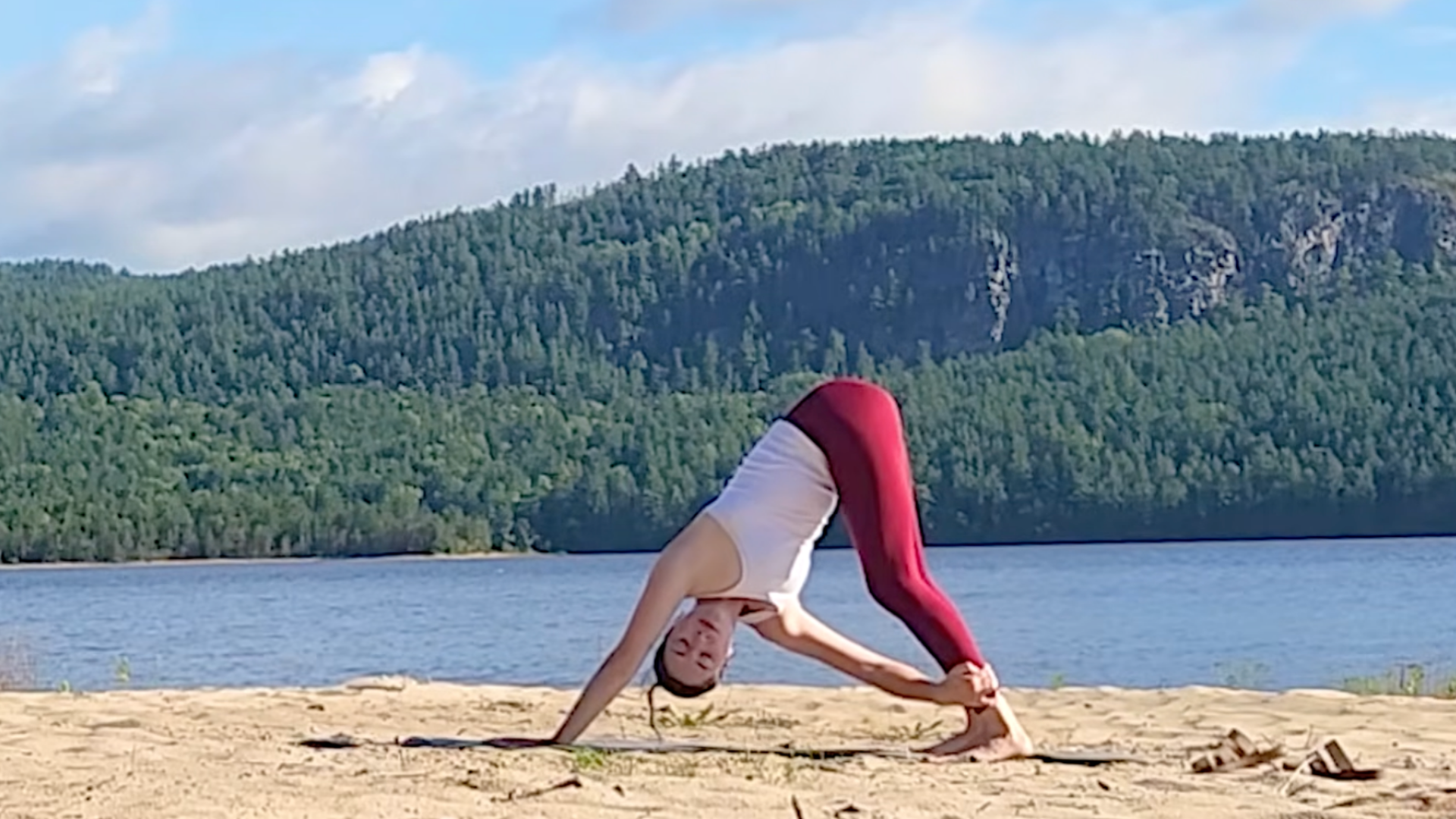 Woman in Downward-Facing Dog (Adho Muka Svanasana) but with a twist by taking her right hand to her outer left ankle