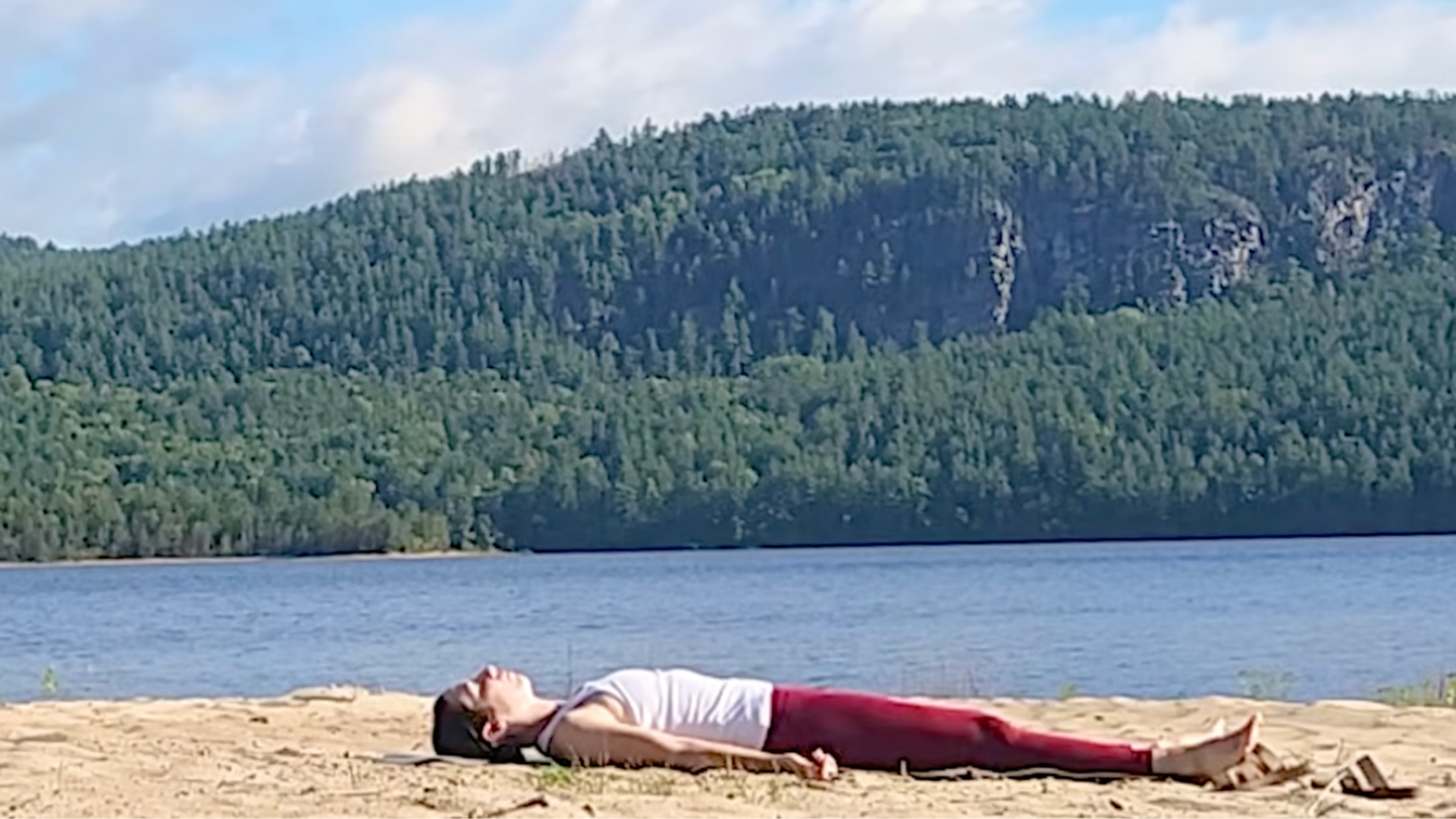 Woman lying in Savasana on the beach against the backdrop of the Canadian mountains 