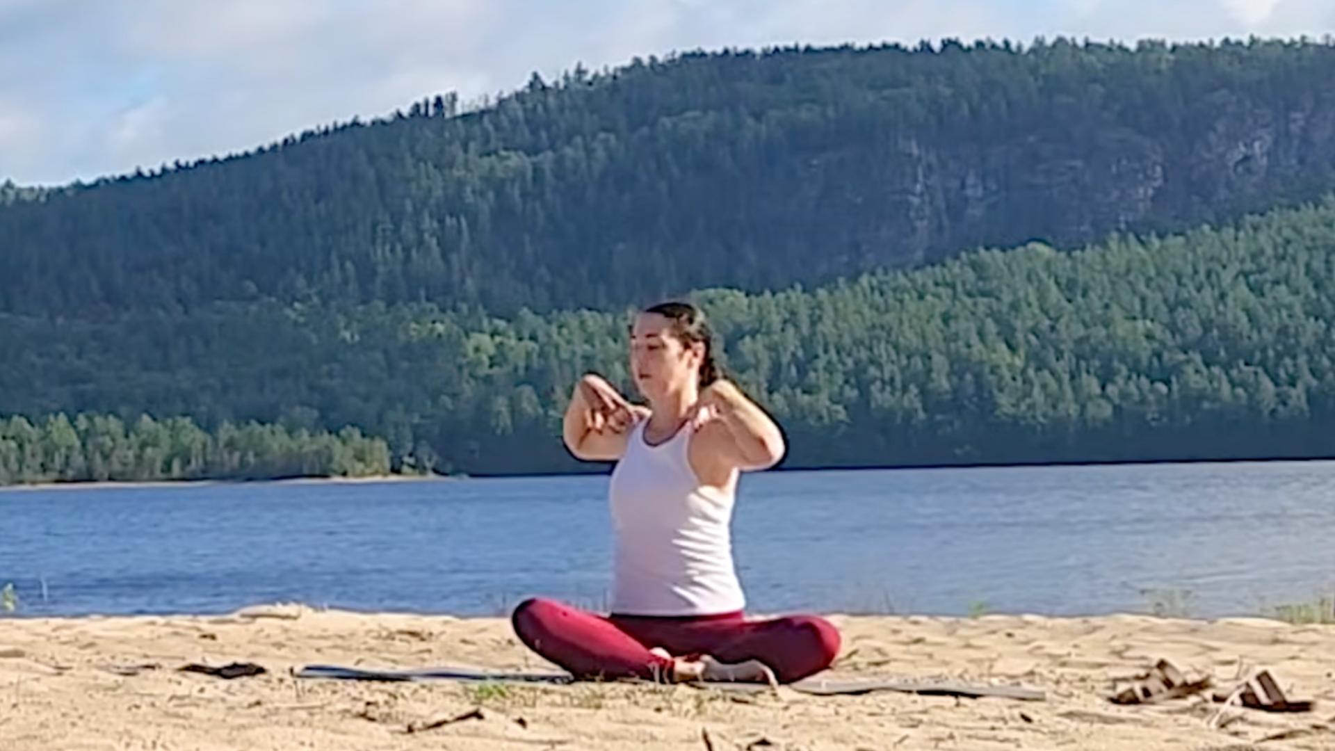 Woman sitting cross-legged with her fingertips on her shoulders as she twists from side to side