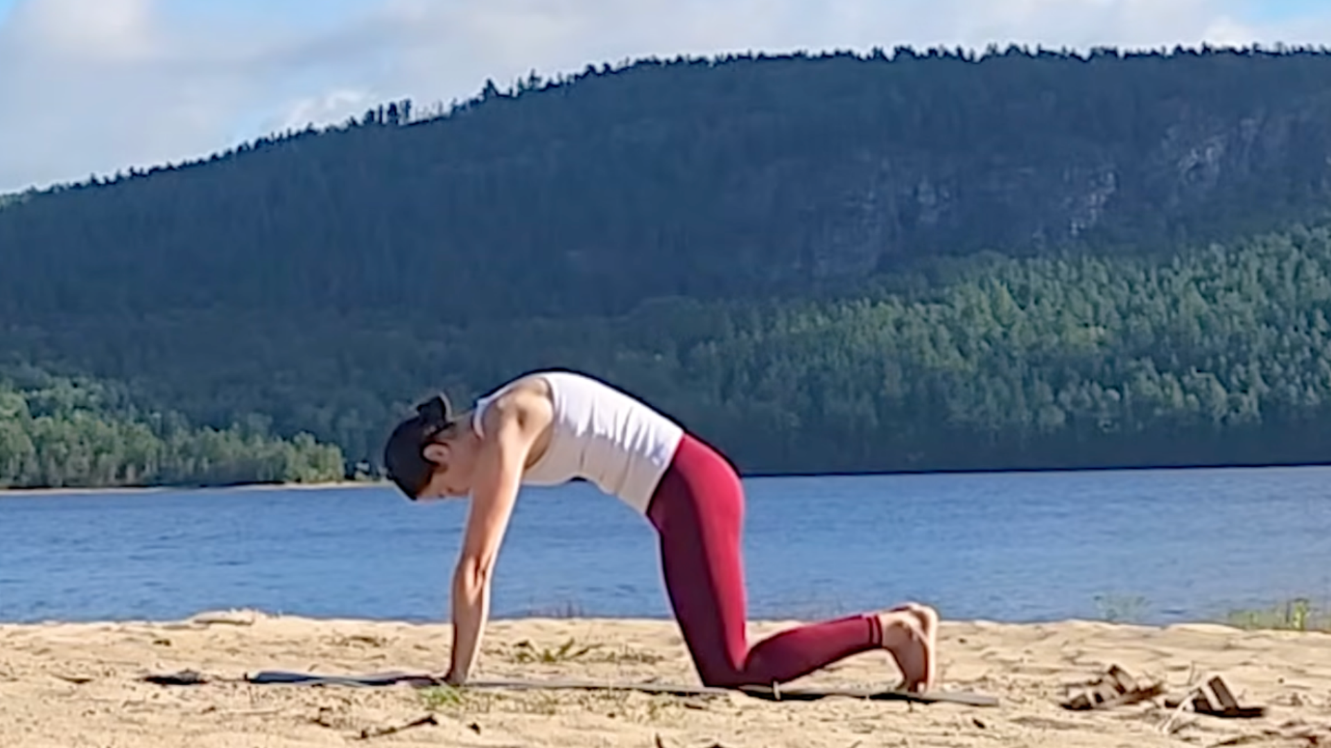 Woman kneeling on a yoga mat during a 15-minute yoga routine in which she's rounding her back in Cat Pose