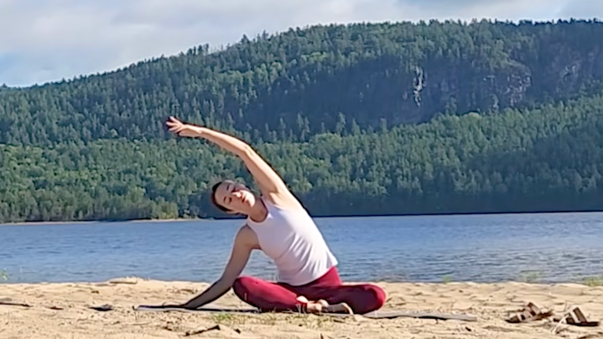 Yoga teacher sitting cross-legged and leaning to her right in a seated side bend