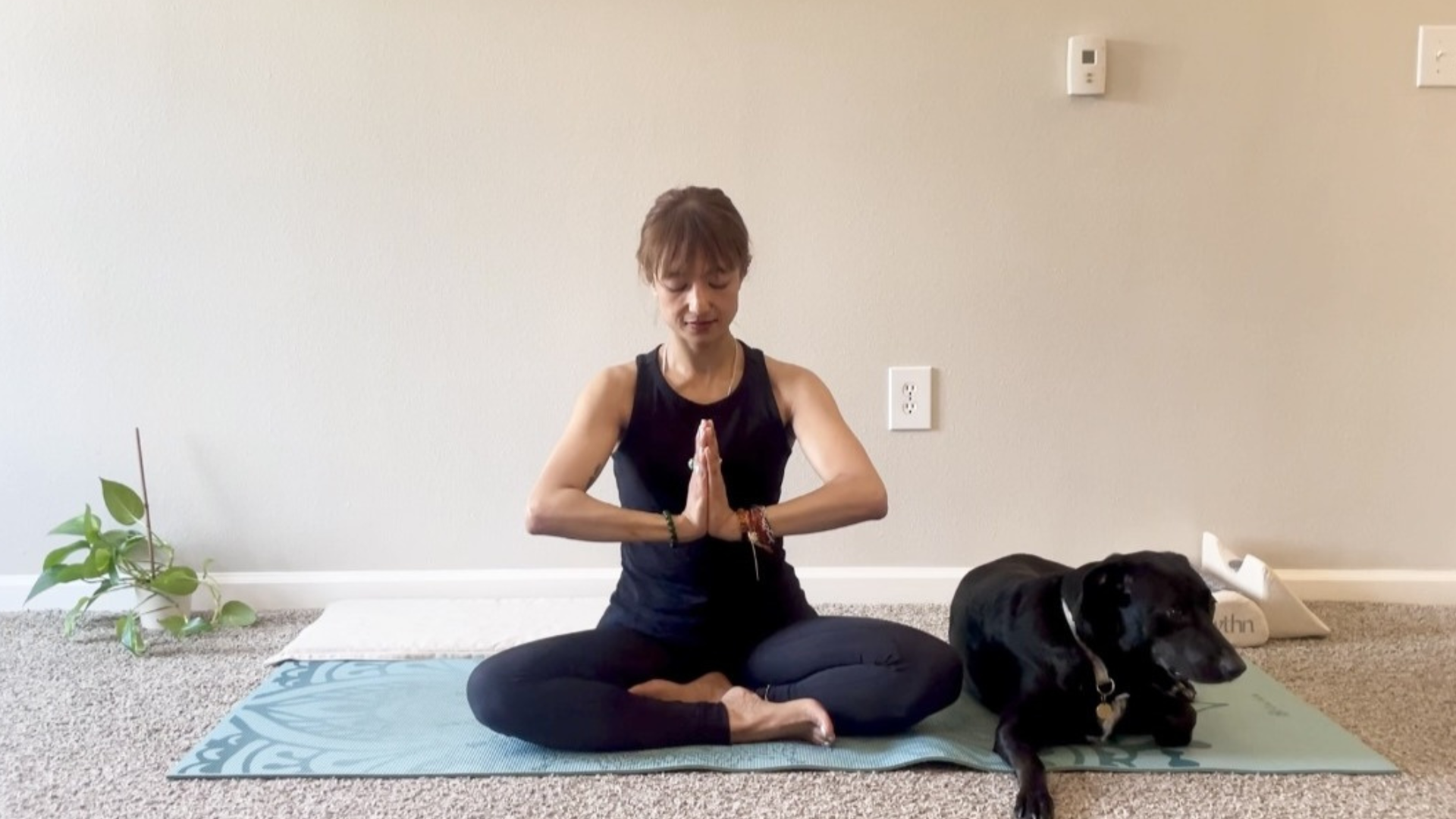 Woman sitting with her palms together in anjali mudra while pressing them together isometrically for wrist strengthening exercises