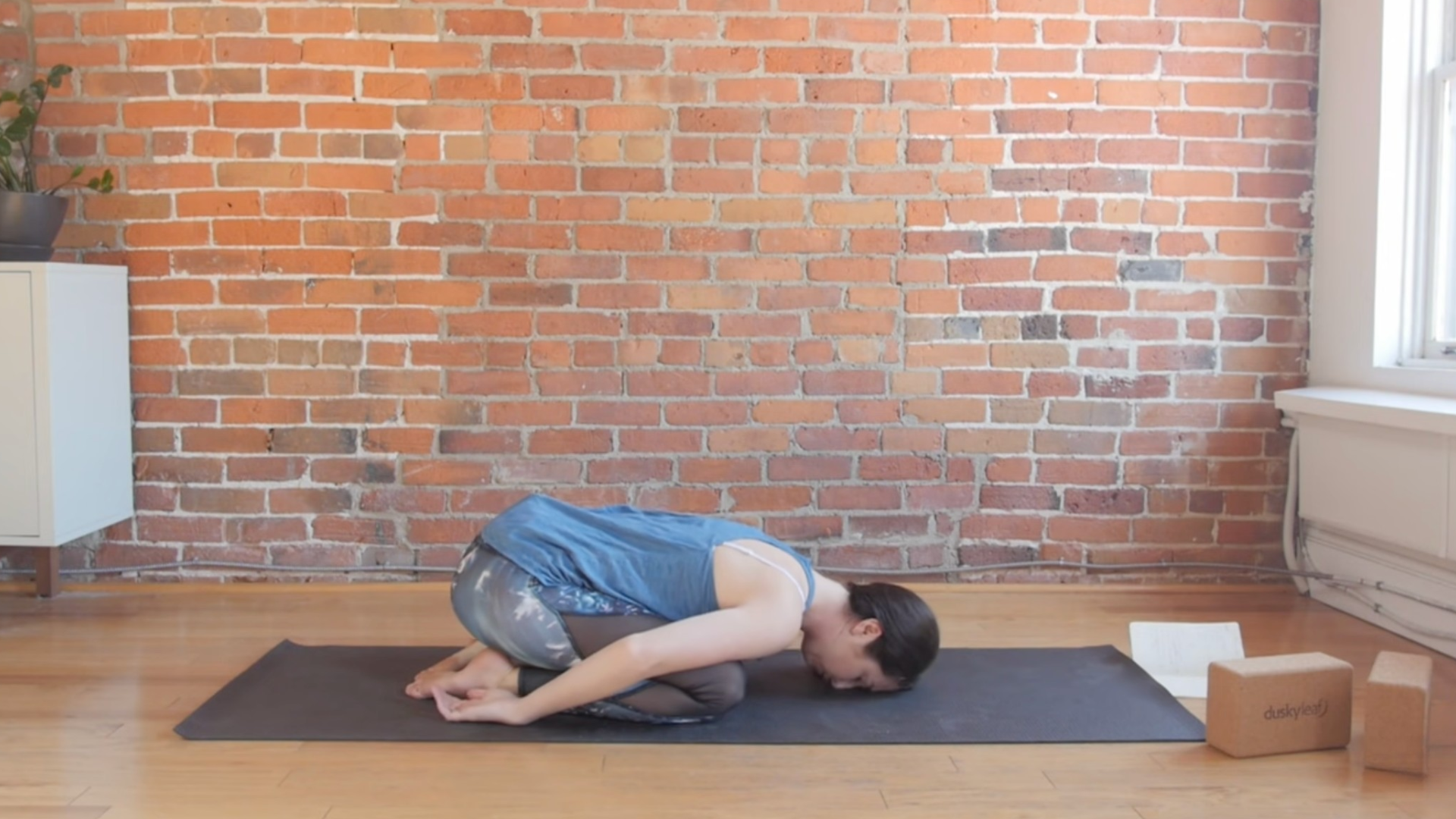 Woman kneeling on a yoga mat and leaning forward in Child's Pose with her forehead, or Third Eye chakra or Ajna on the mat