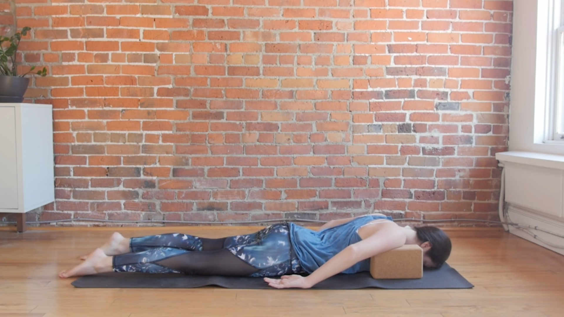 Woman lying on her belly with blocks beneath her shoulders in the yin yoga pose known as Crocodile Pose