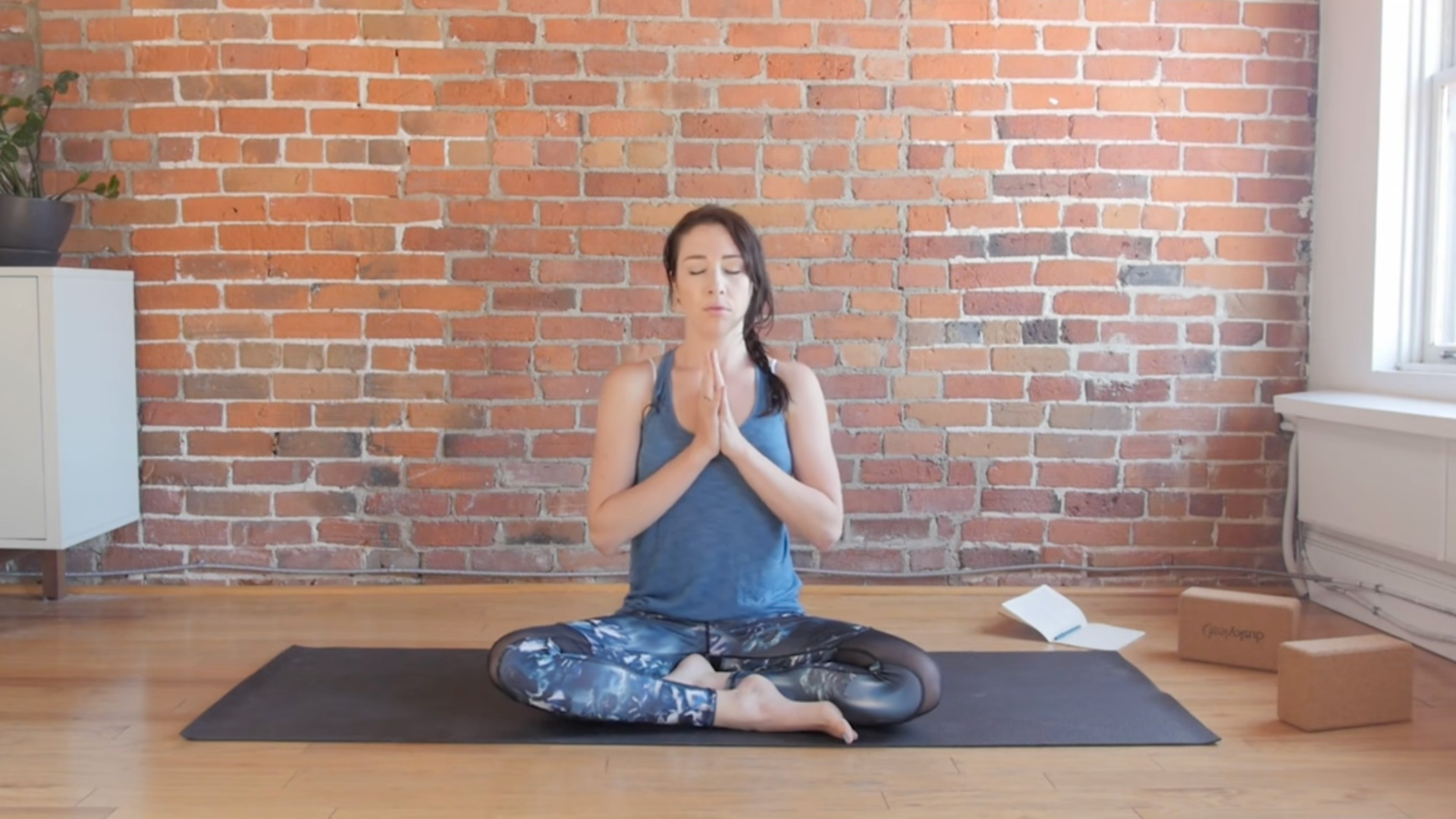 Woman sitting in meditation with her hands together at her chest in prayer hands, or Anjali mudra