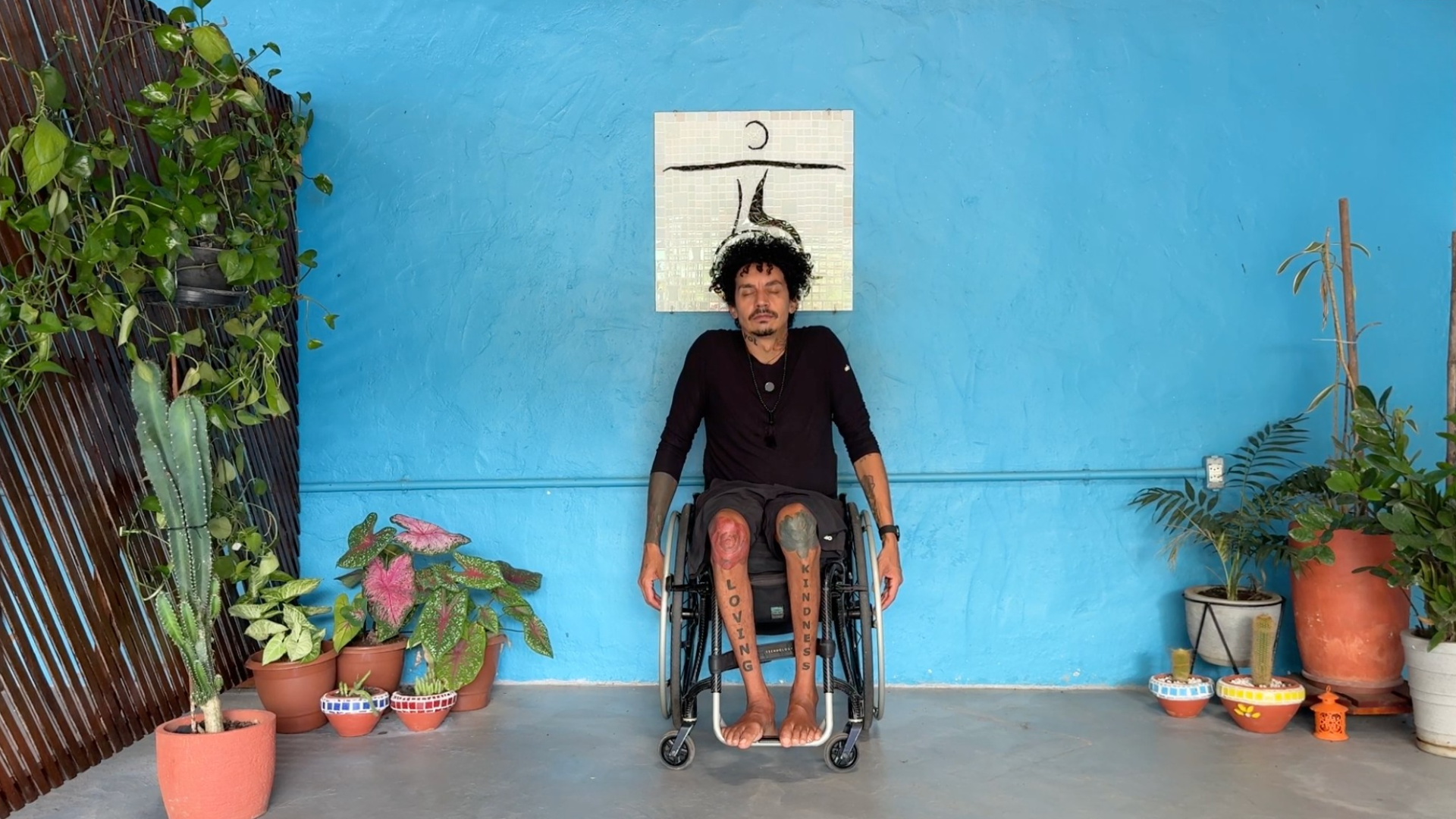 Man seated in a wheelchair during a 20-minute yoga routine doing shoulder shrugs