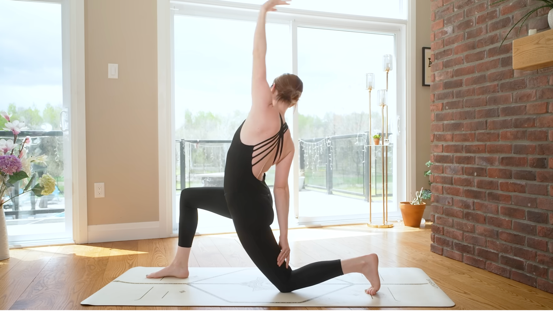 A woman kneels on a yoga mat with her arm reaching up and her arm down her back thigh