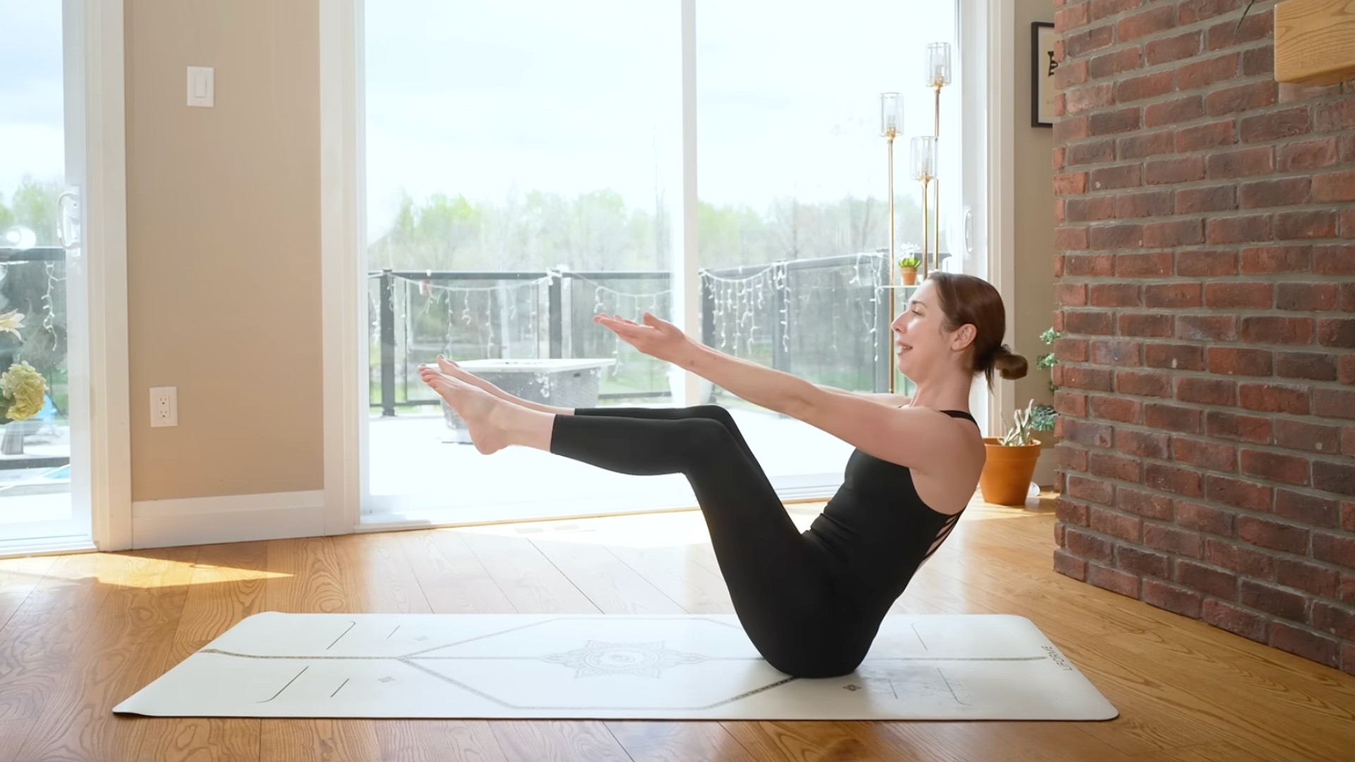 A woman sits on a yoga mat with her legs raised and arms extended in boat pose or Navasana