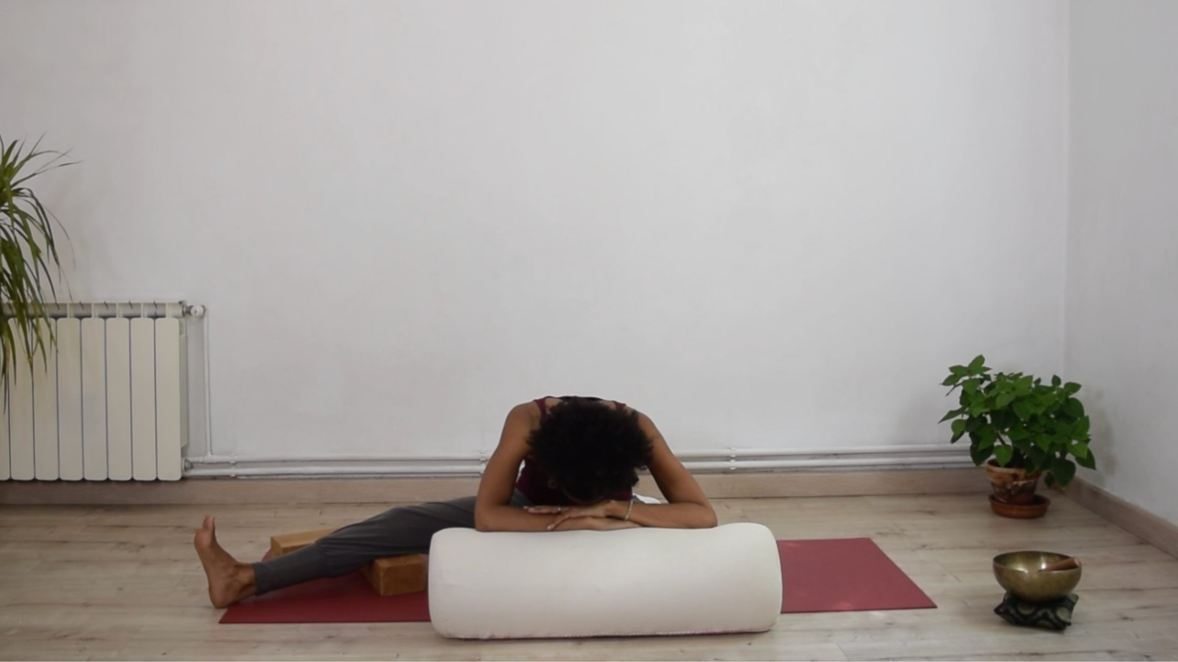 A person sitting with one leg extended outward and the opposite foot drawn in, folding forward with hands resting on a bolster.