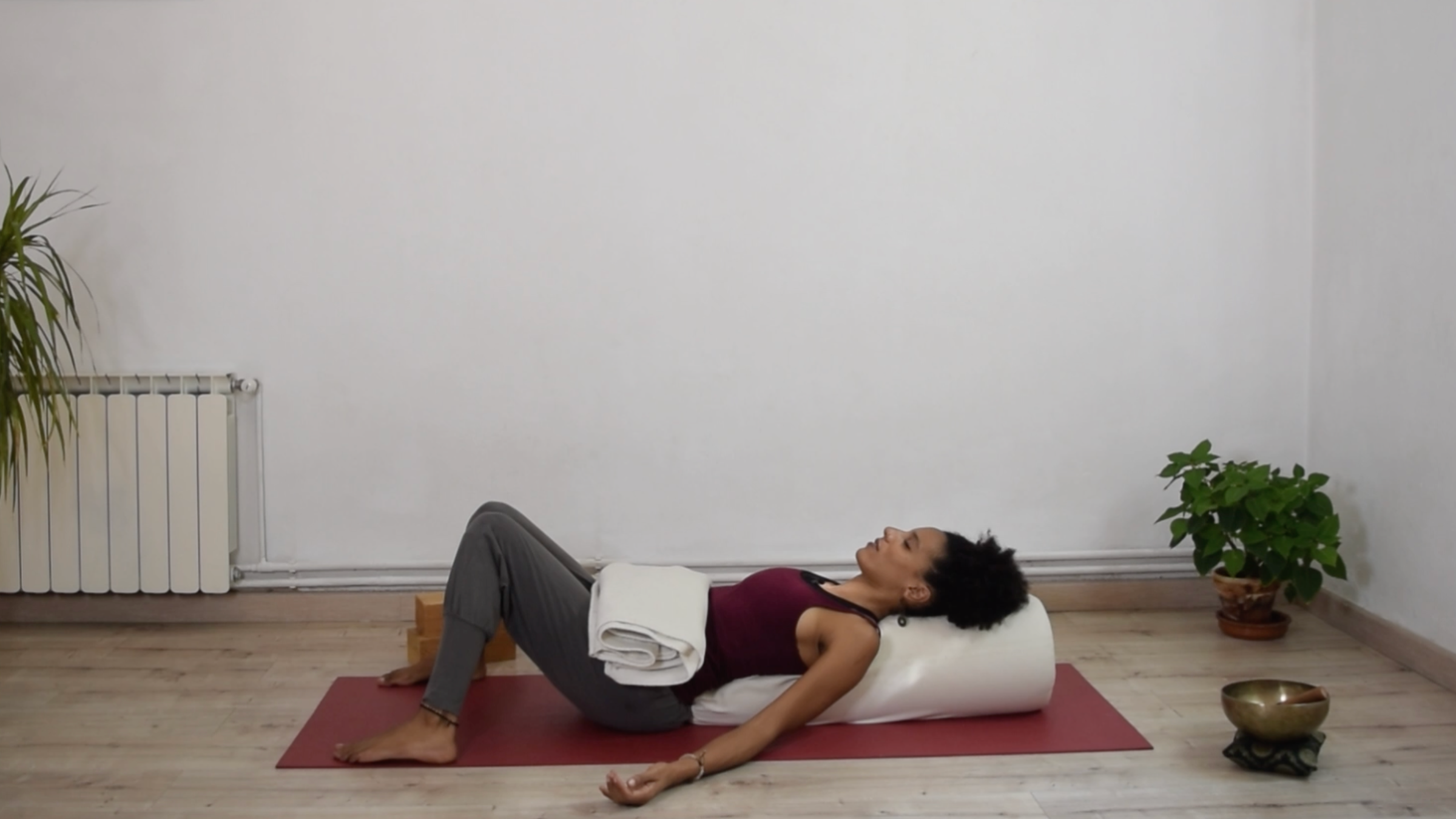 A person lying back onto a lengthwise bolster with knees bent and resting inward against each other, palms facing up at their sides.