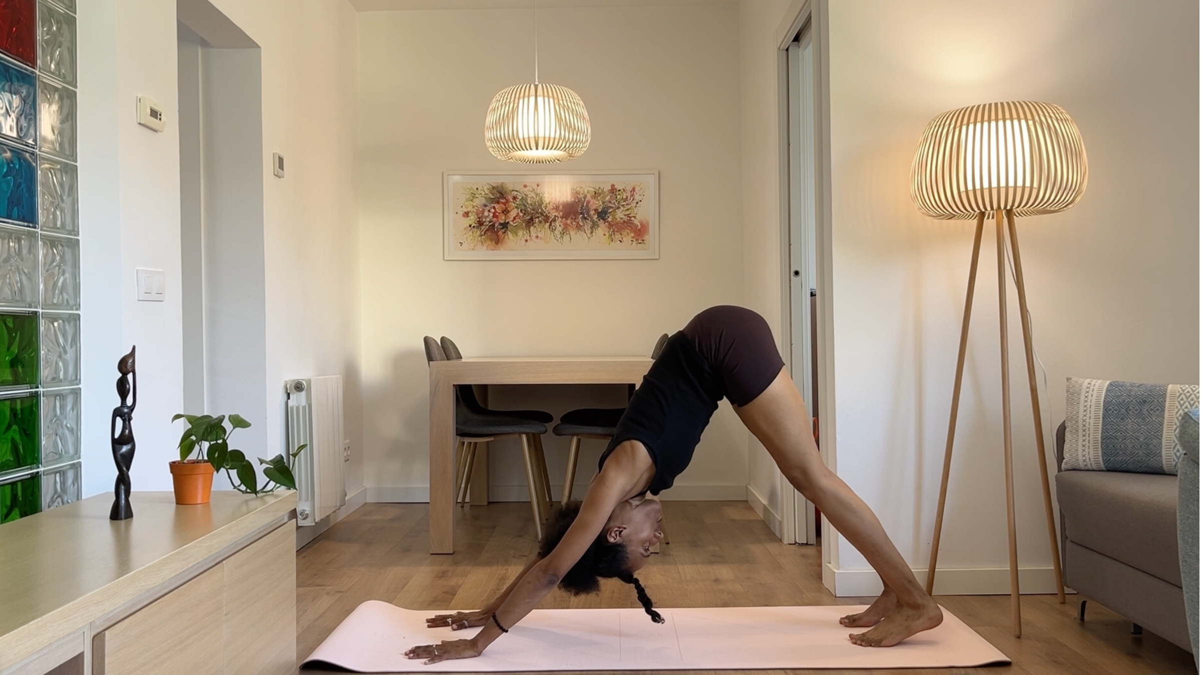 A person in Downward-Facing Dog pose, making an inverted V-shape with their body, hands pressing firmly into the mat, hips lifted high, and heels reaching toward the floor.