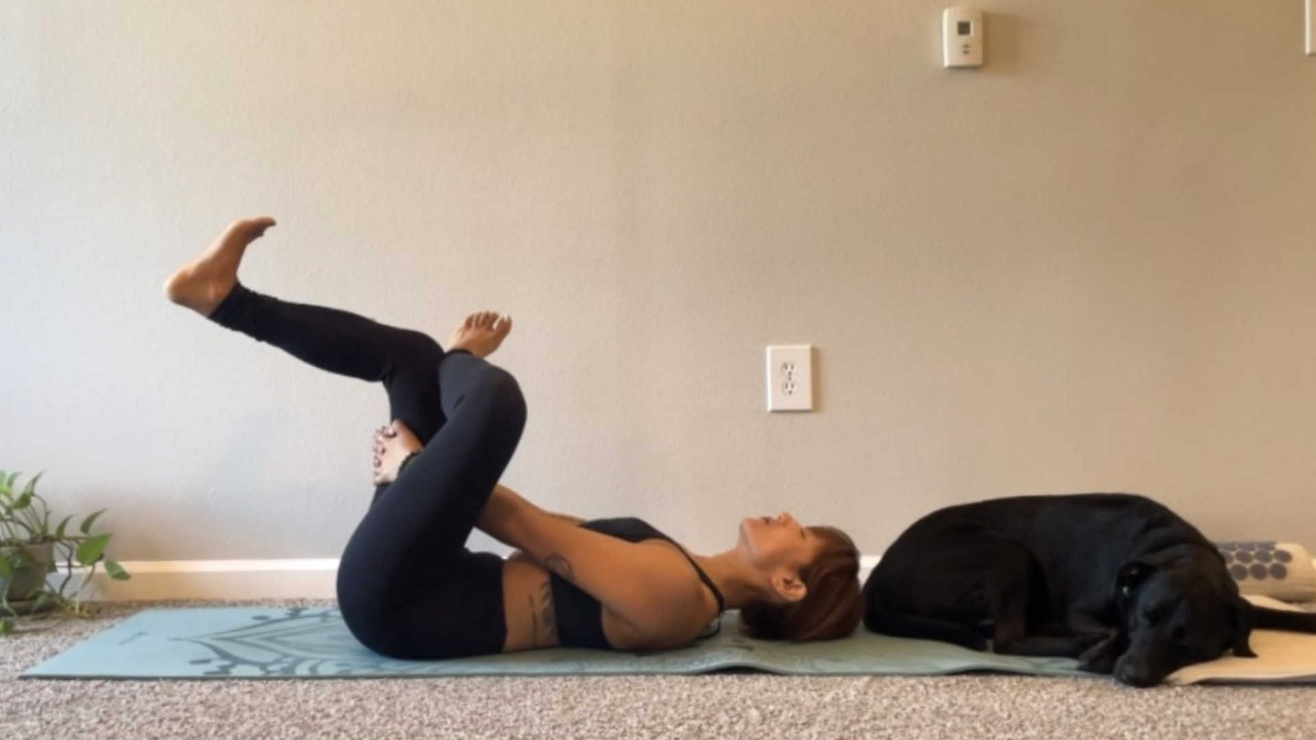 Woman in a version of Reclined Figure 4 while lying on a yoga mat with her right knee against her left thigh