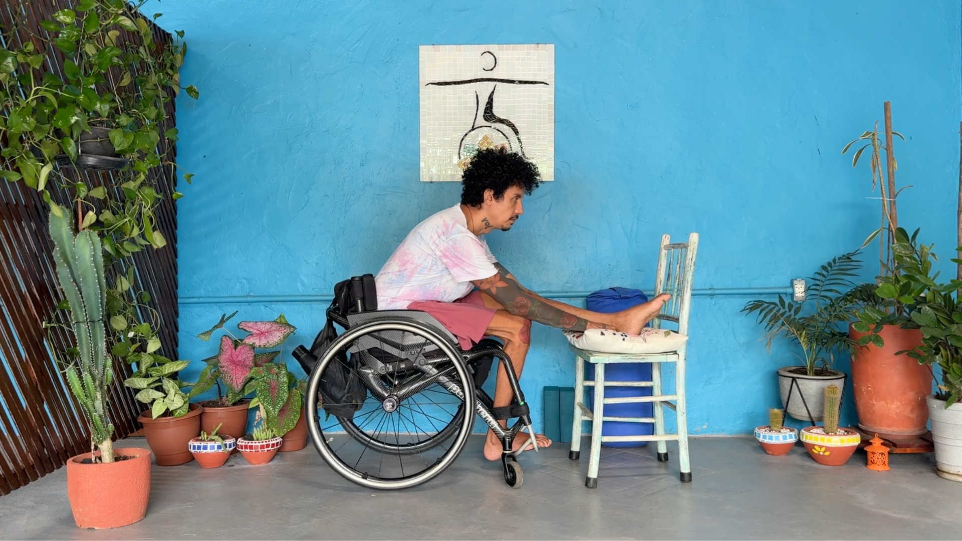 Man in a wheelchair doing a seated forward bend with his right leg on a second chair in front of him in Janu Sirsasana or Seated Forward Bend