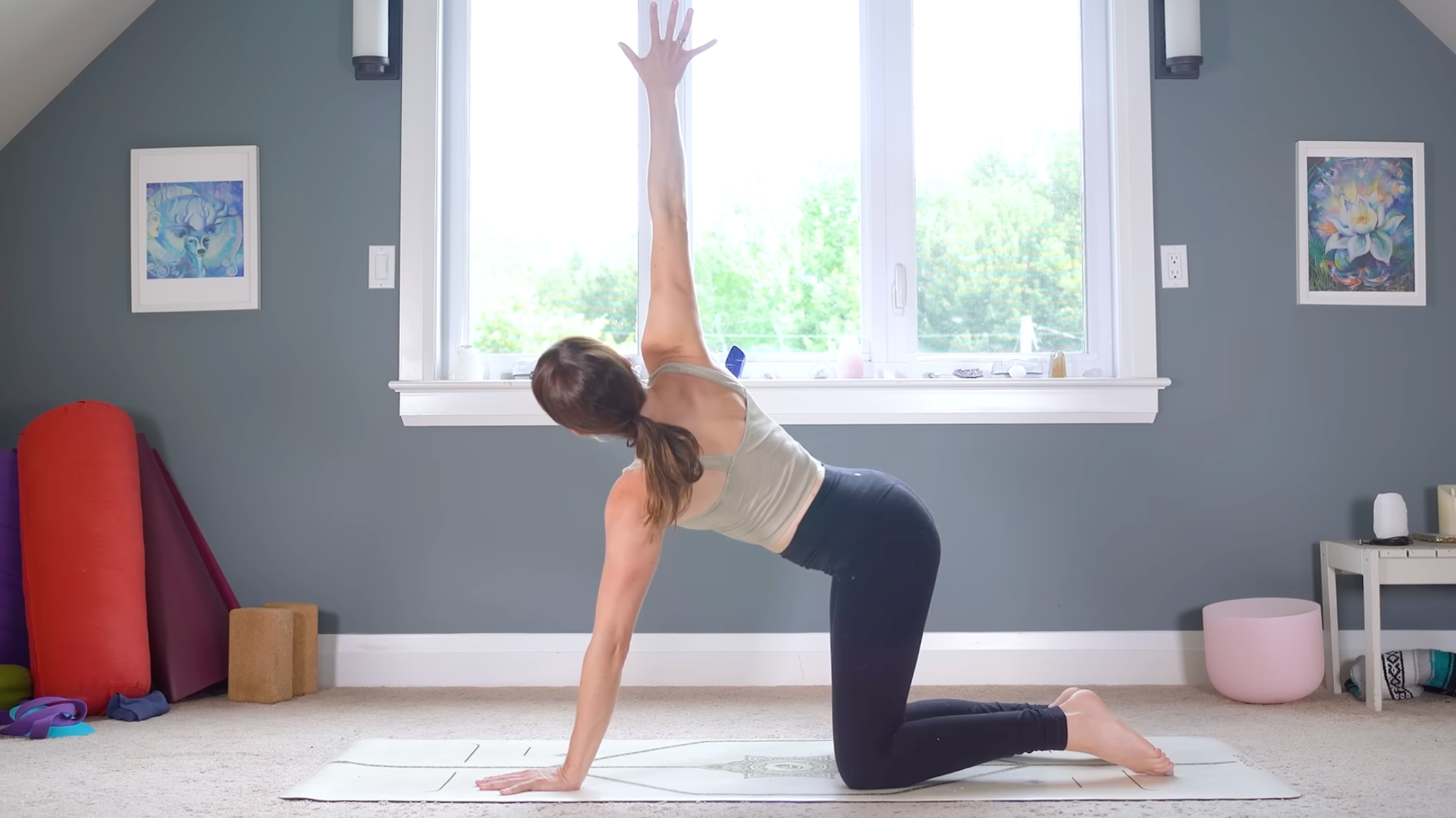 Woman kneeling on a yoga mat with her right arm reaching toward the ceiling