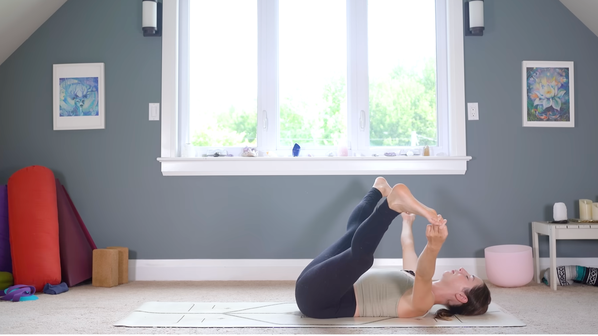 Woman lying on her back on a yoga mat in a straight-leg version of Happy Baby or Ananda Balasana