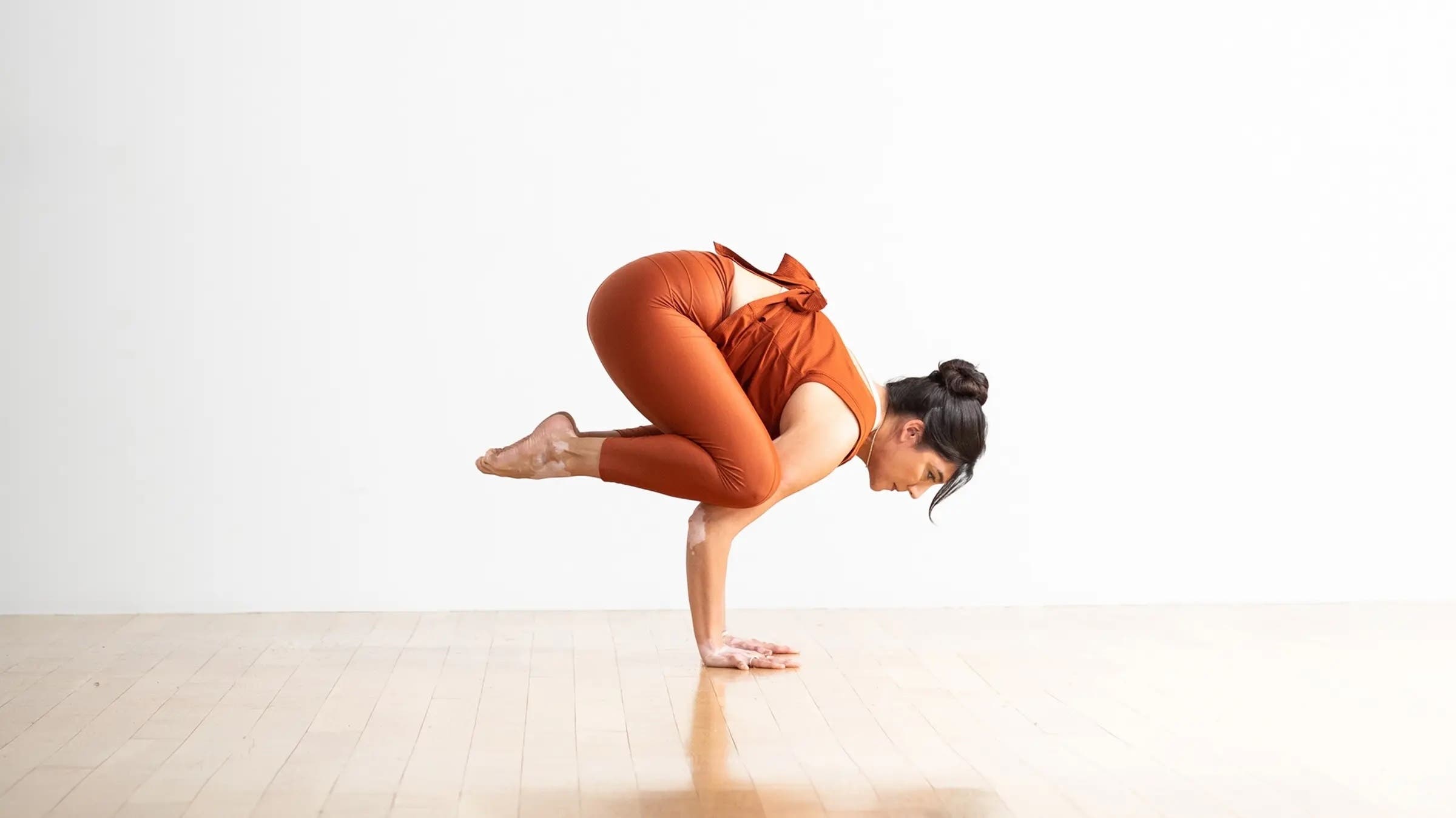 A woman in Crow Pose, a yoga pose for strong arms