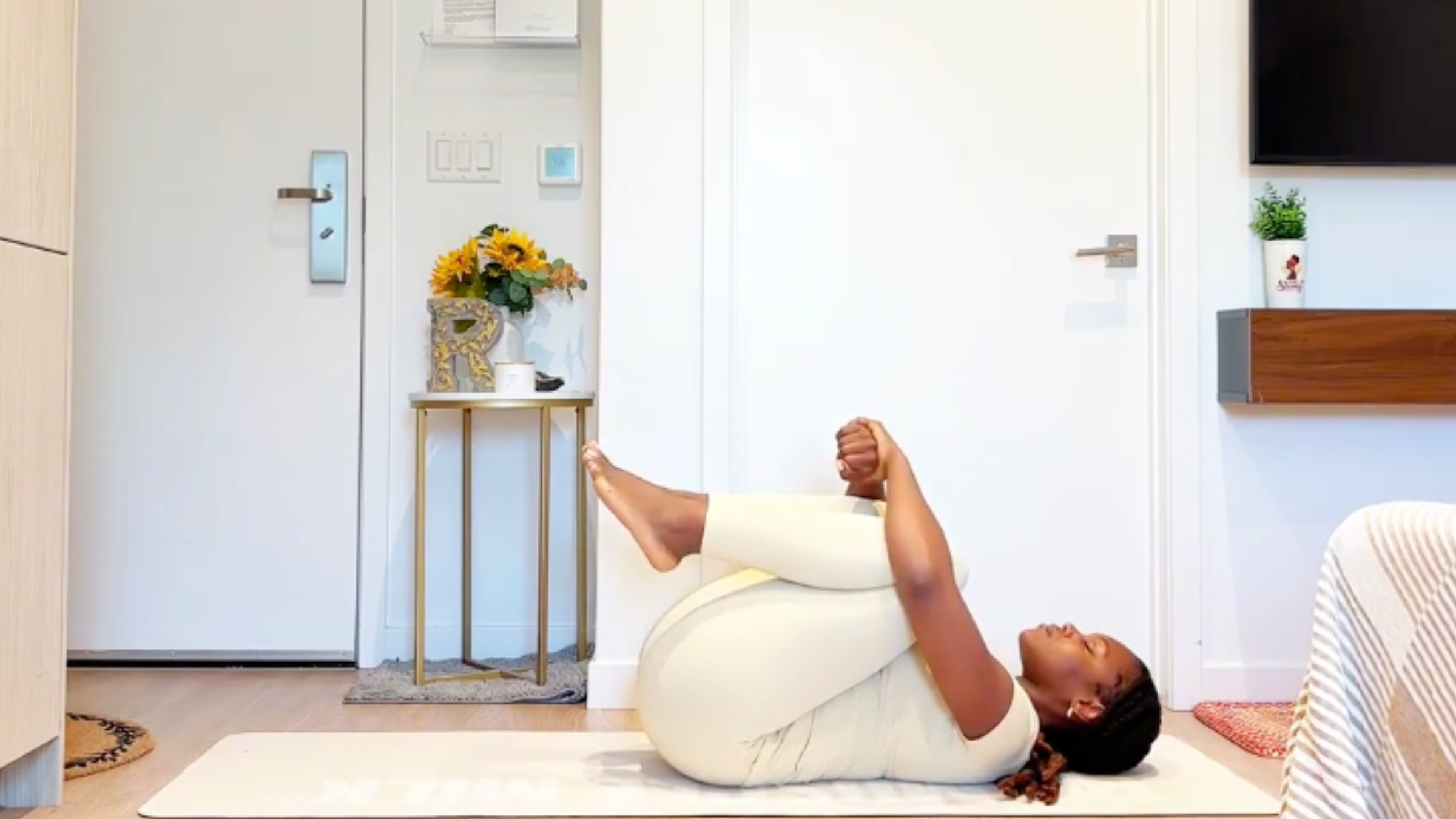 Yoga instructor Ramoni Overton lying on back, drawing both knees toward her chest and hugging her shins with both hands.