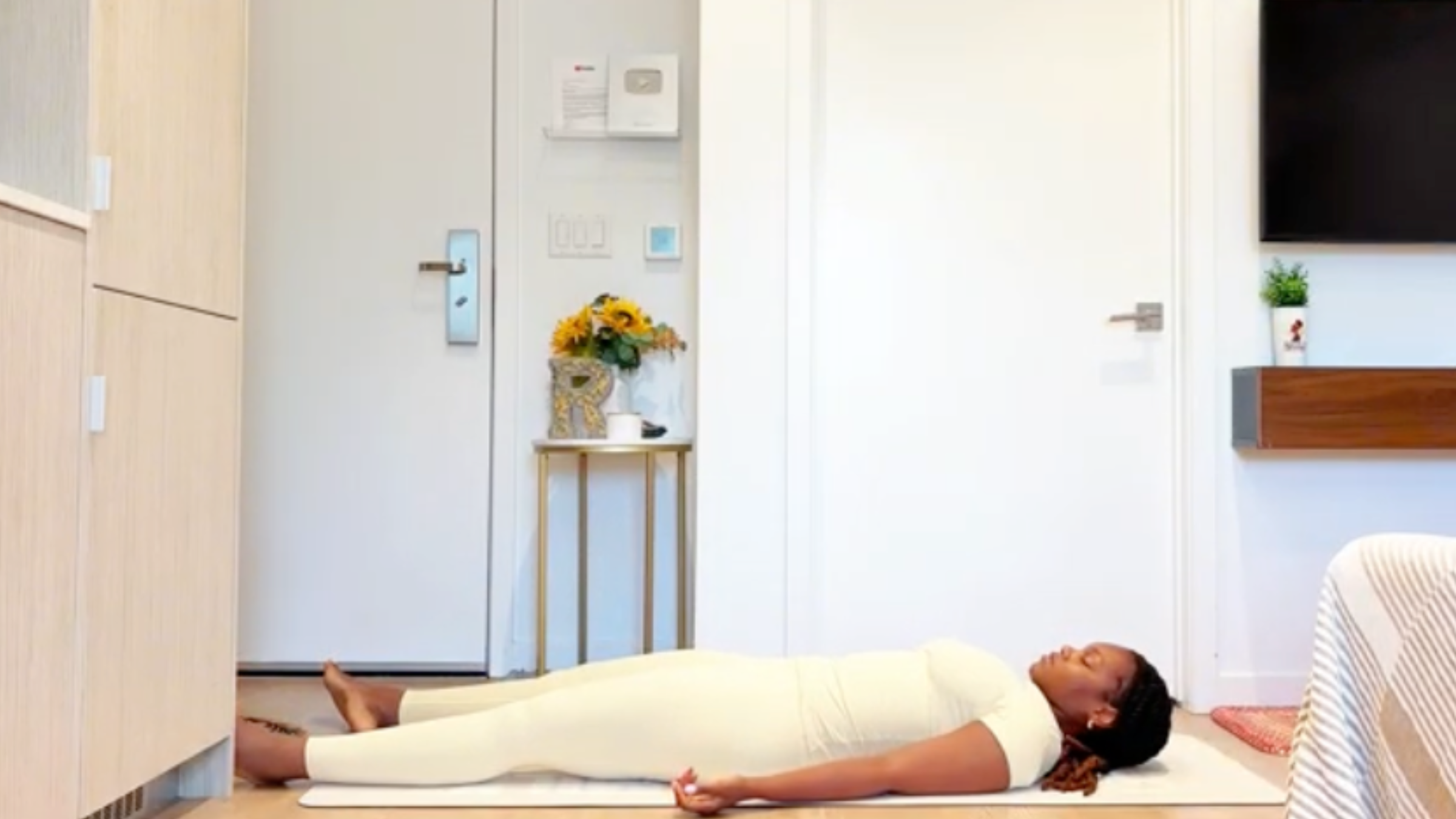 Yoga instructor Ramoni Overton lying fully extended on back on a yoga mat with arms and legs relaxed, palms facing up, and eyes gently closed.