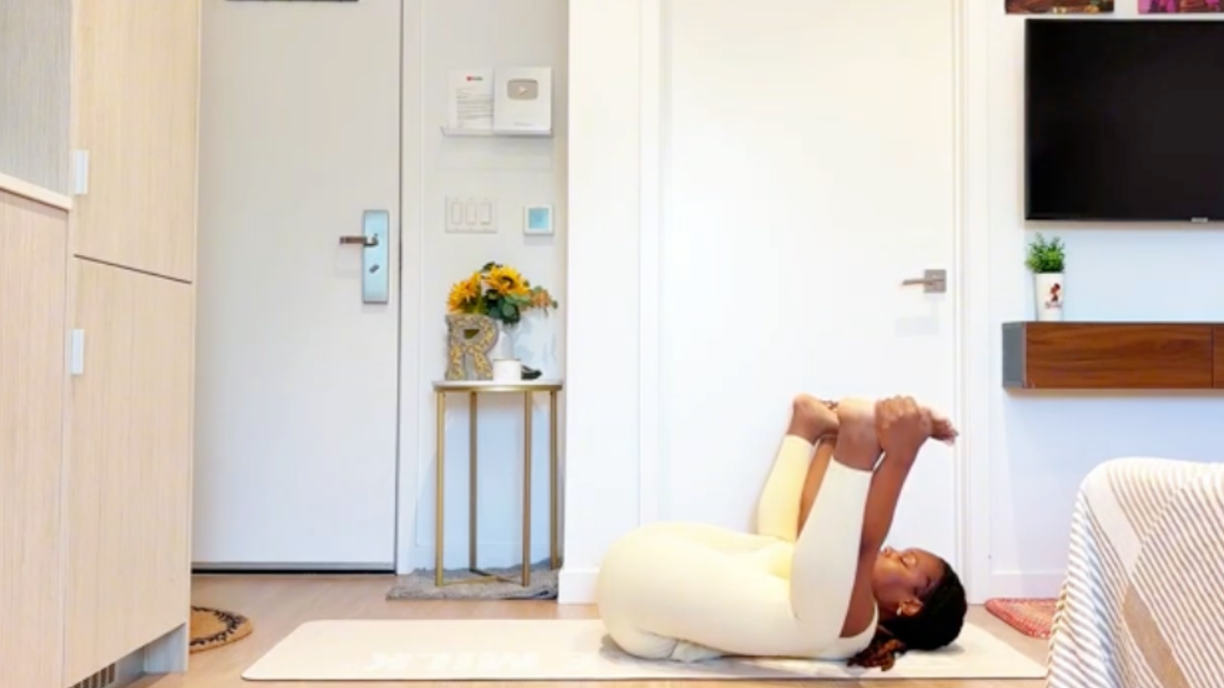 Yoga instructor Ramoni Overton lying on back holding the outer edges of her feet with knees bent deeply toward her armpits and soles facing upward.