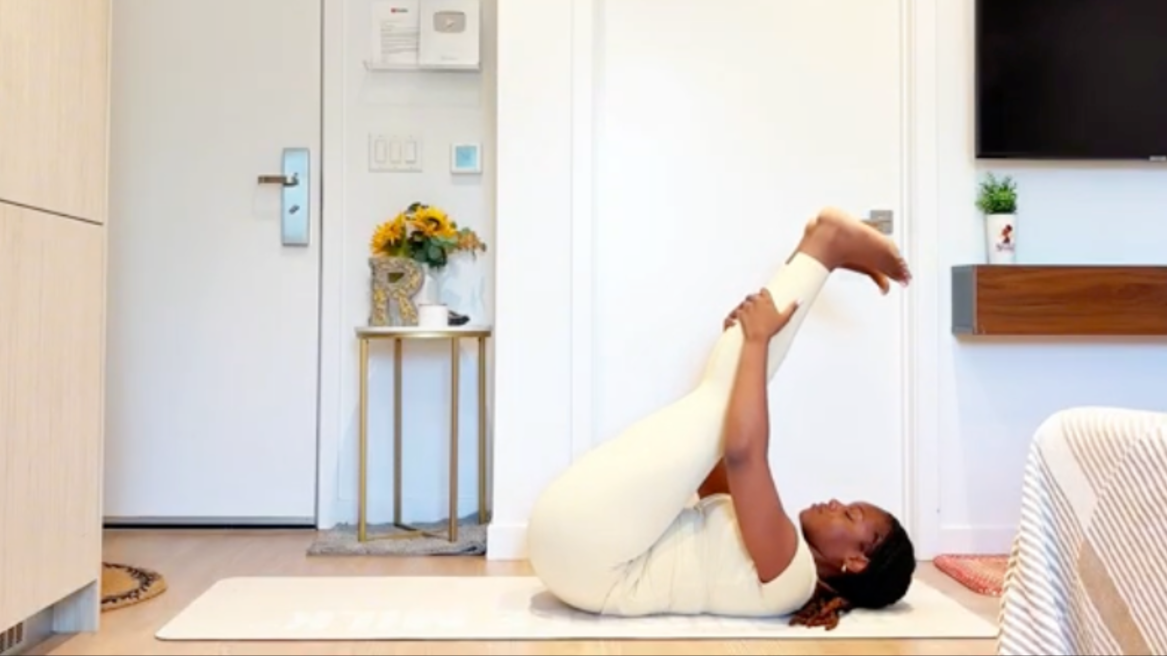 Yoga instructor Ramoni Overton lying on back extending both legs up toward the ceiling, gently pulling legs toward torso while keeping lower back grounded.