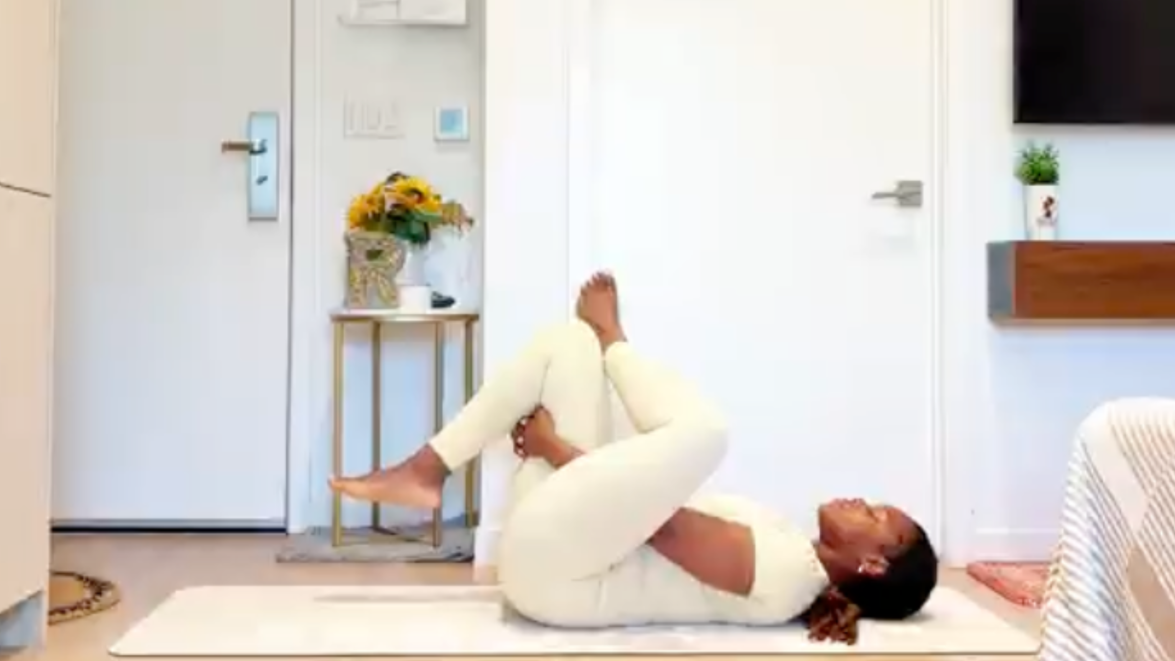 Yoga instructor Ramoni Overton lying on back with knees bent, crossing her left ankle over her right knee and reaching hands to hold behind her right thigh.