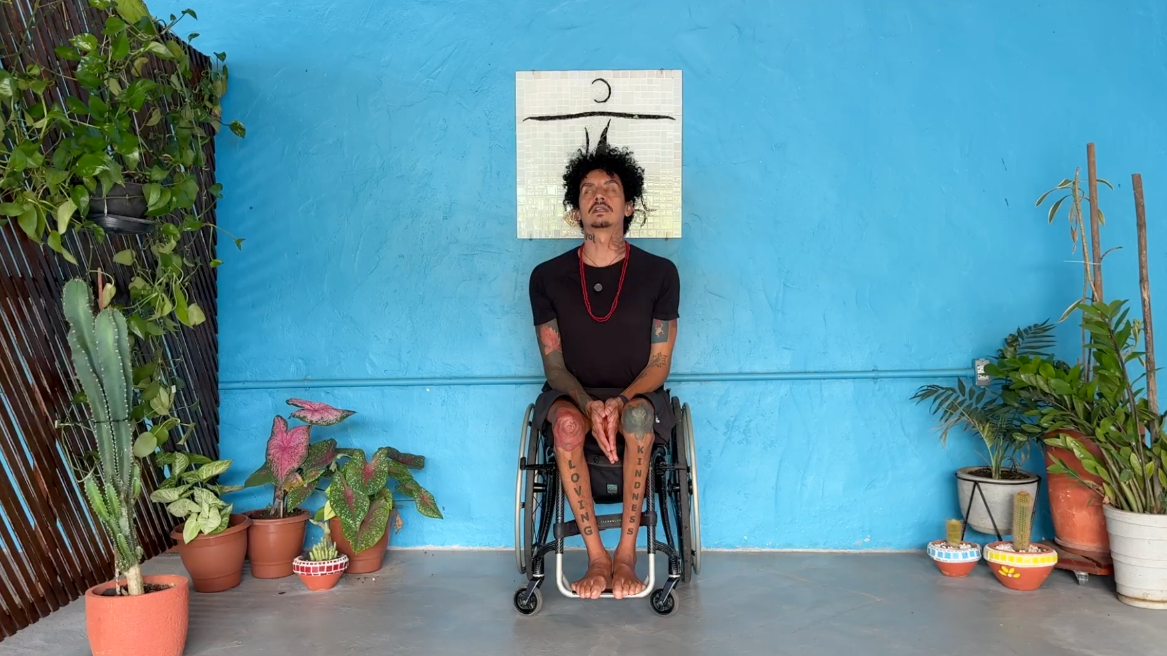 man seated in wheelchair facing camera in Seated Spinal Extension with palms together between knees, back straightened with shoulder blades back and face looking up
