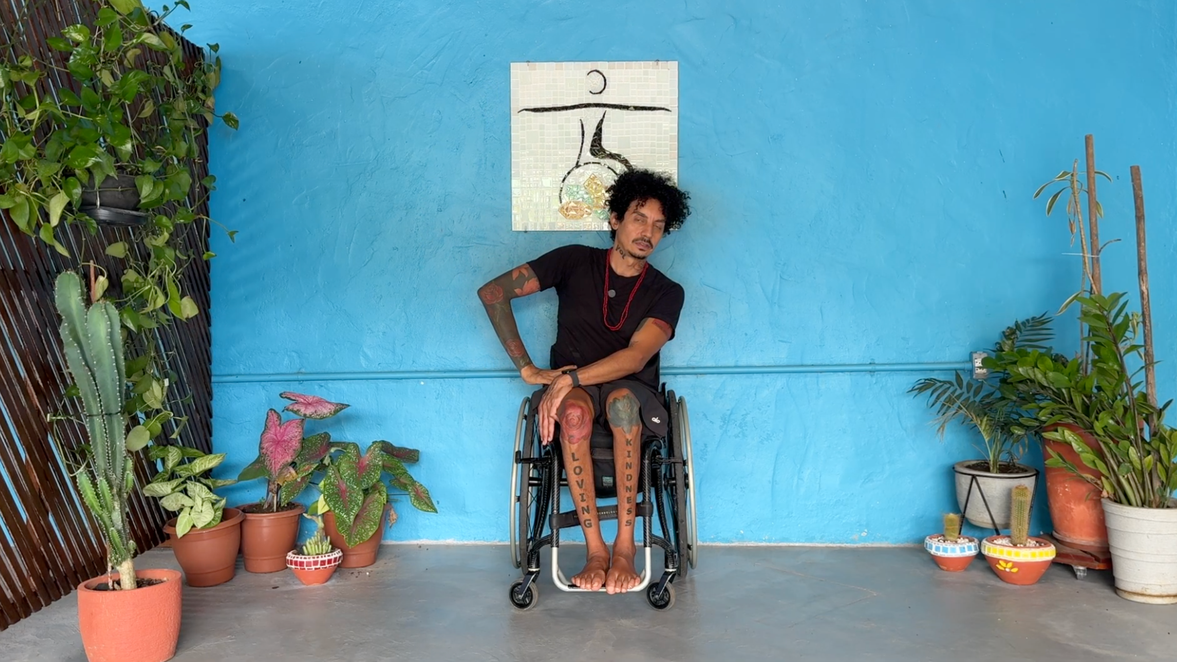 man seated in wheelchair in Seated Side Bend with left arm crossed to outside of right knee and right hand on hip with body bending toward left side