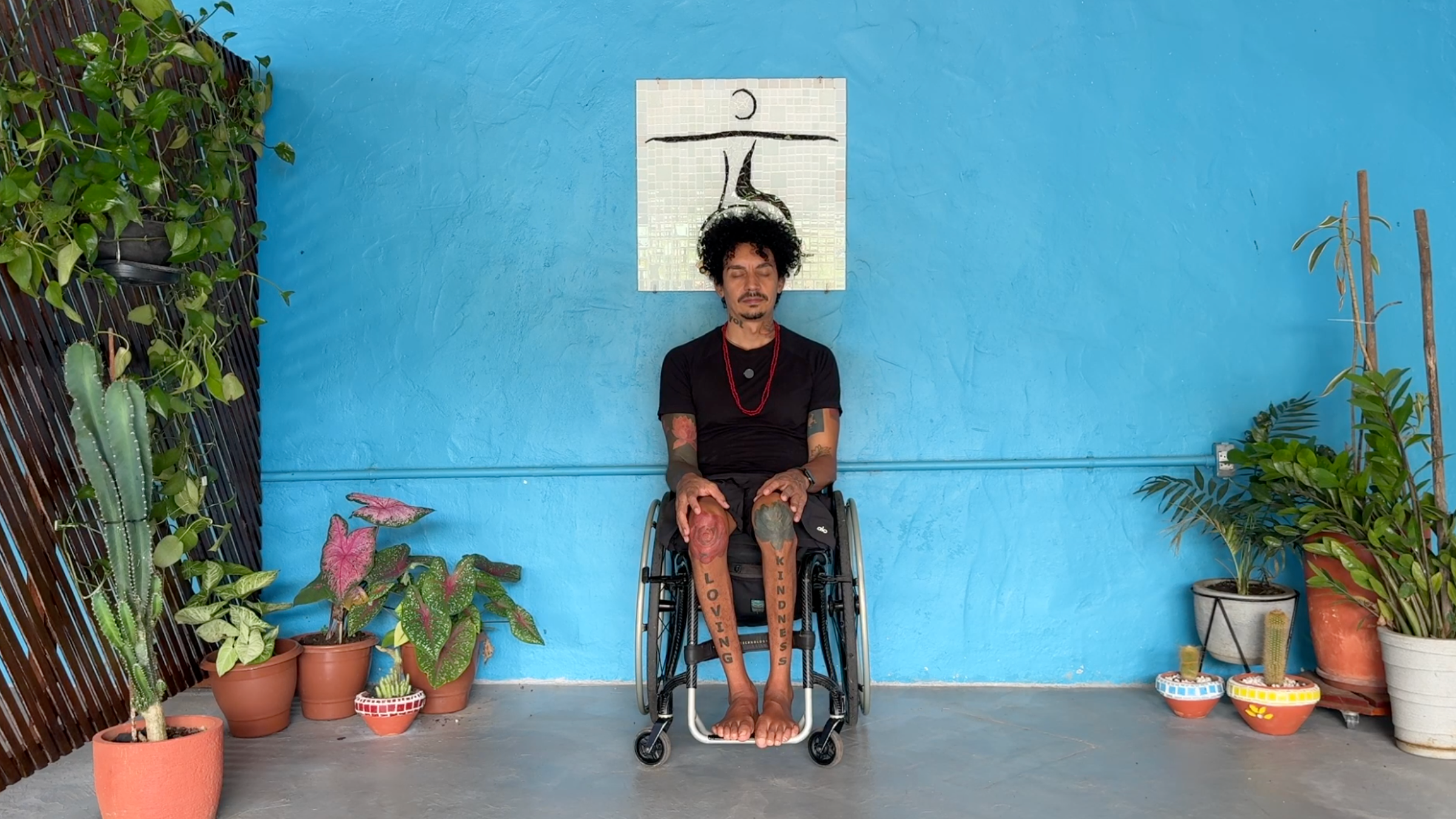 man seated in wheelchair facing camera in Closing pose with hands resting on knees and eyes closed