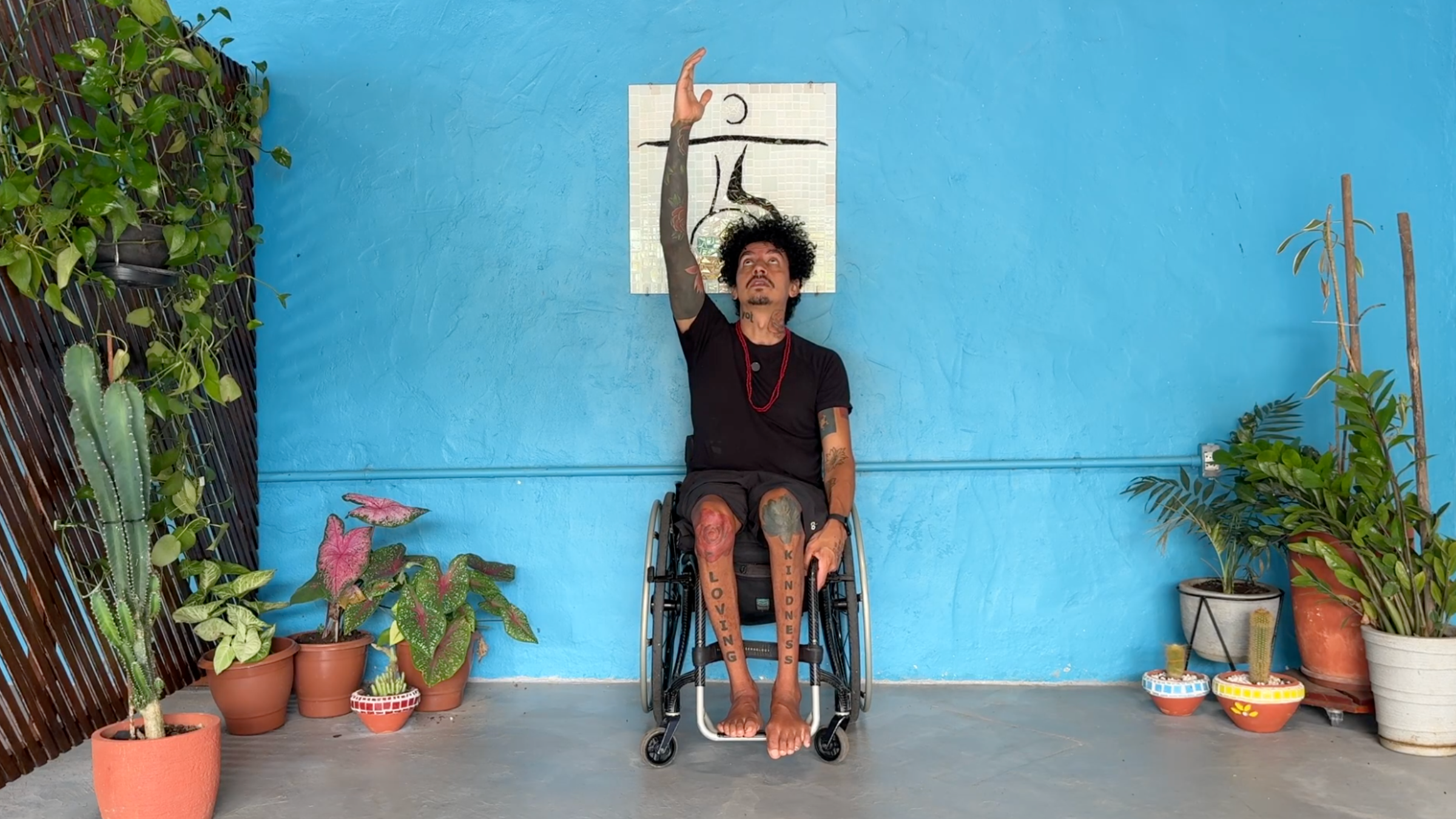 man in wheelchair in neck and shoulder stretch with left hand grabbing chair frame and right arm raised toward the sky with eyes and face lifted to look at hand