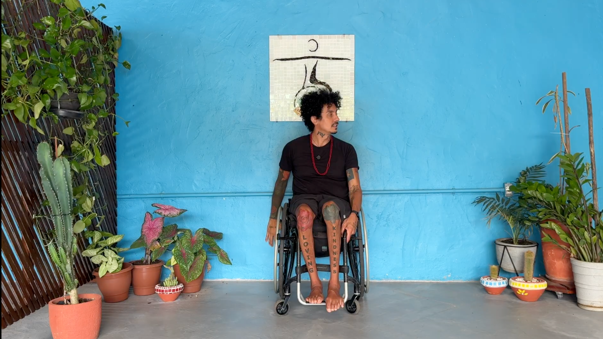 man in wheelchair in Neck Stretch pose left arm grabbing chair frame, right arm extended down with palm toward wall, and face looking over left shoulder