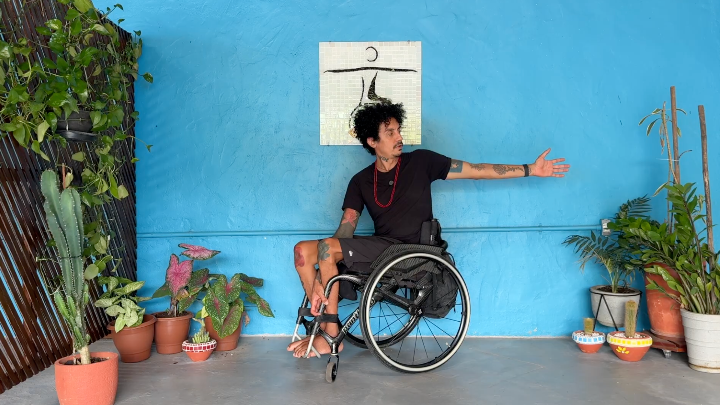 man in wheelchair facing toward his right in Seated Twist with left arm extended behind him and right hand gripping chair frame between legs and face looking toward left hand