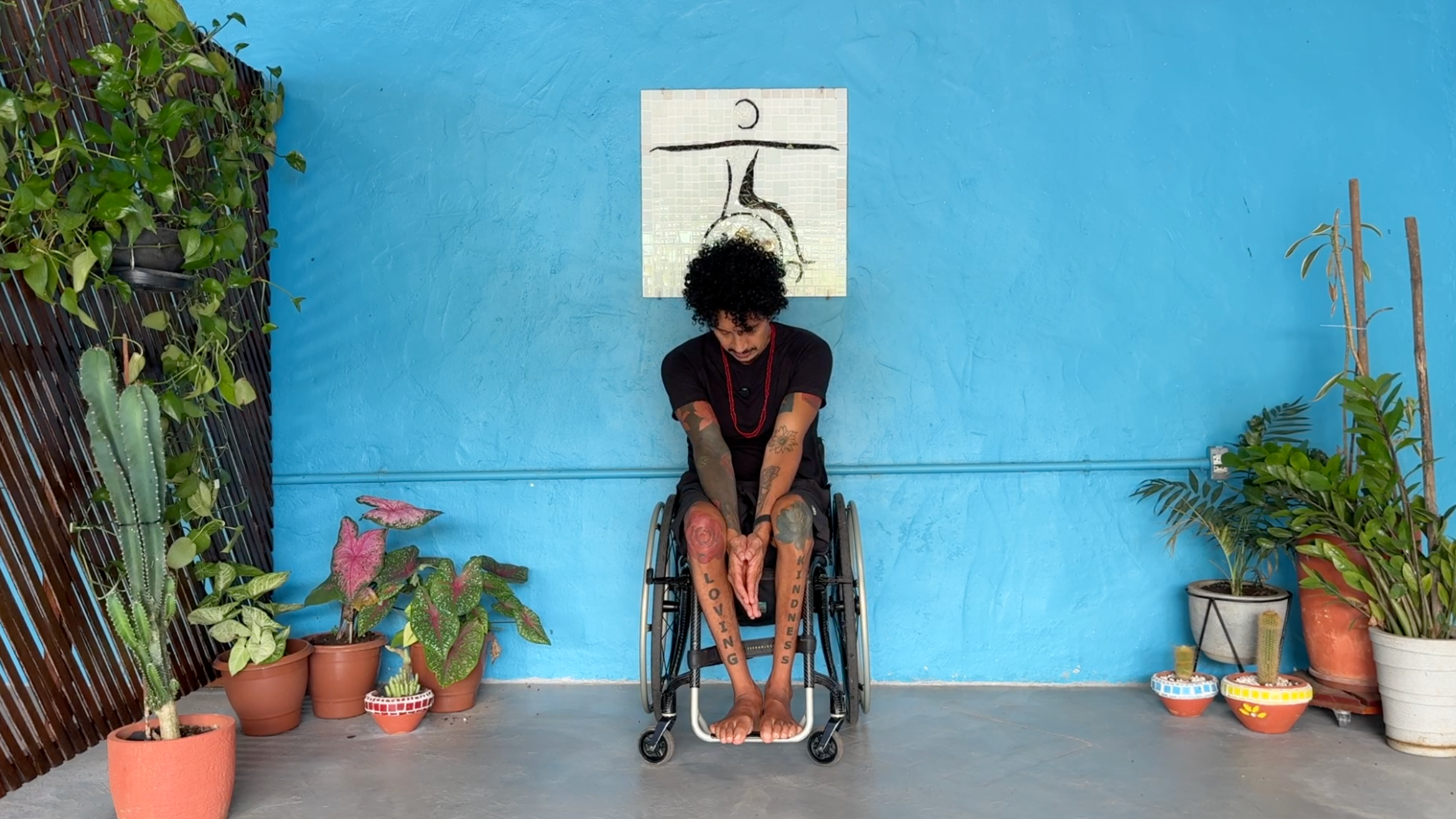 man in wheelchair facing toward camera in Seated Spinal Flexion with palms together between knees, arms straight, bending forward with chin tucked and face looking down