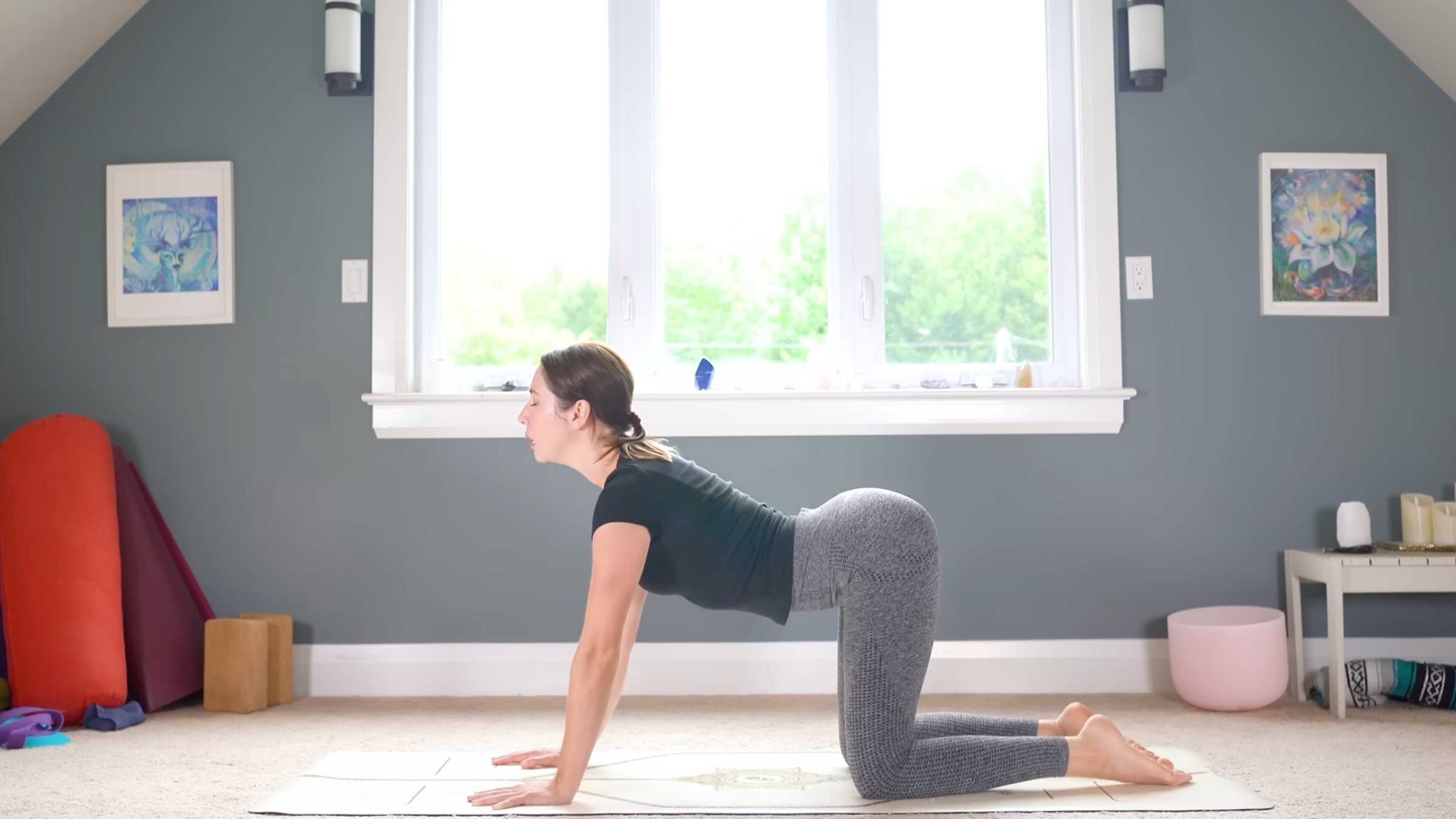 woman in yoga clothes on hands and knees in Cow pose with belly lowered and face forward on carpeted floor in home