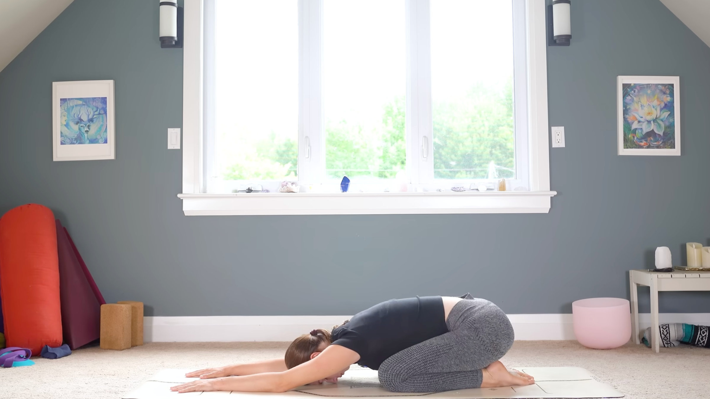 woman in yoga clothes in Child Pose on yoga mat sitting on heels with forehead on mat and arms extended forward, on carpeted floor in home